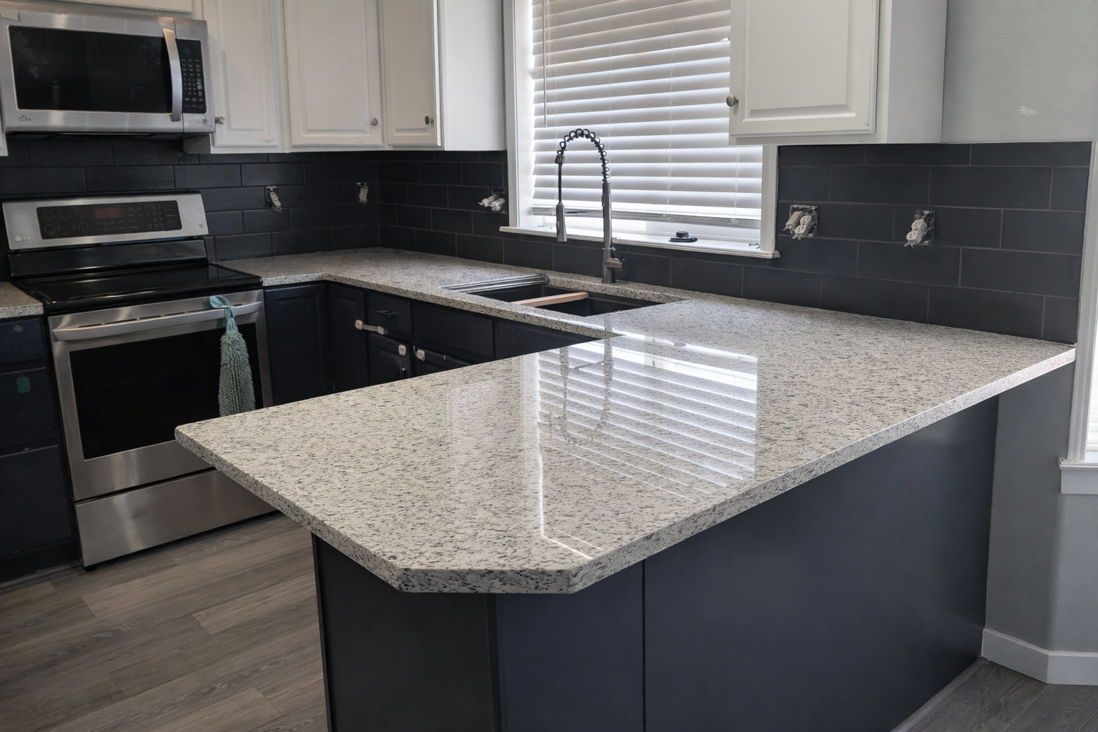 Kitchen with white upper cabinets, black lower cabinets, granite countertops, a stainless steel oven and microwave, and a window with white blinds above the sink.
