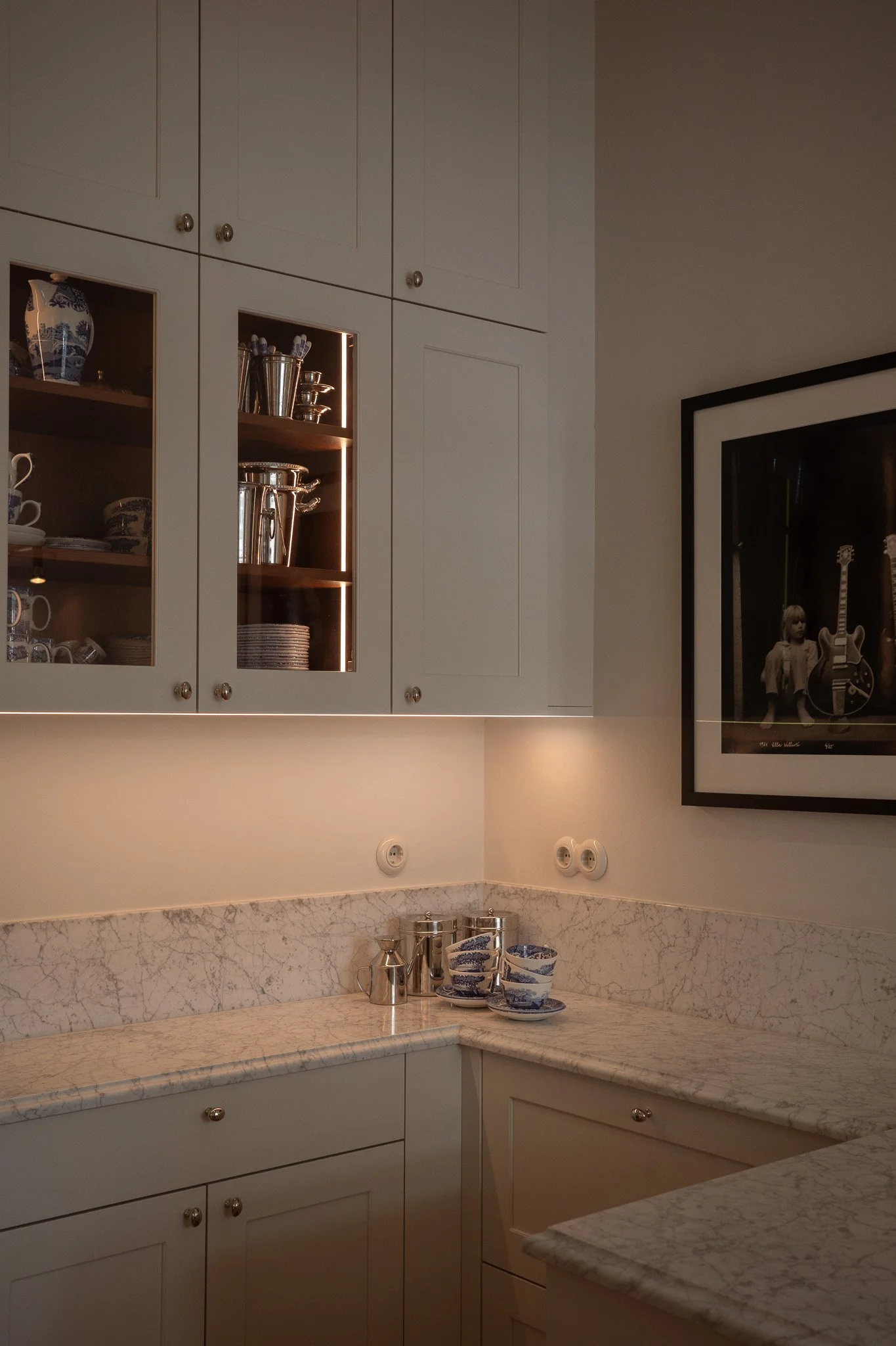 Kitchen with cream-colored cabinets, marble countertops, and a framed photo of a child with musical instruments on the wall.
