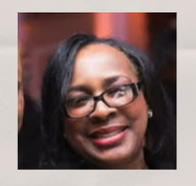 Close-up of a smiling woman with glasses, black hair, and earrings in an indoor setting.