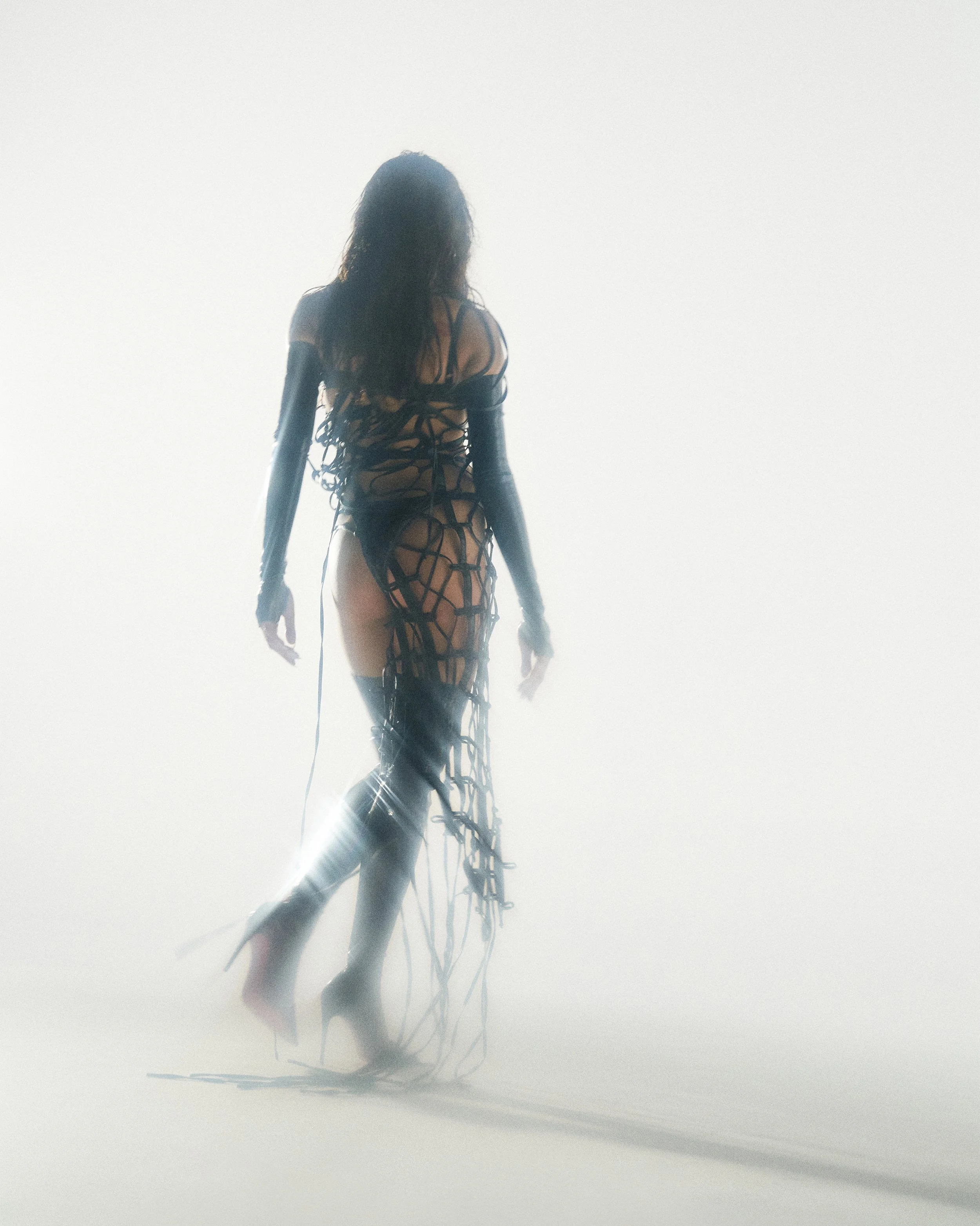 Danna cover for her album Xtasis 2022. Shot by Rafael Arroyo Director and DP based in NY. A person in an intricate, wire-frame outfit standing against a bright, foggy background with sunlight creating a silhouette and long shadow.