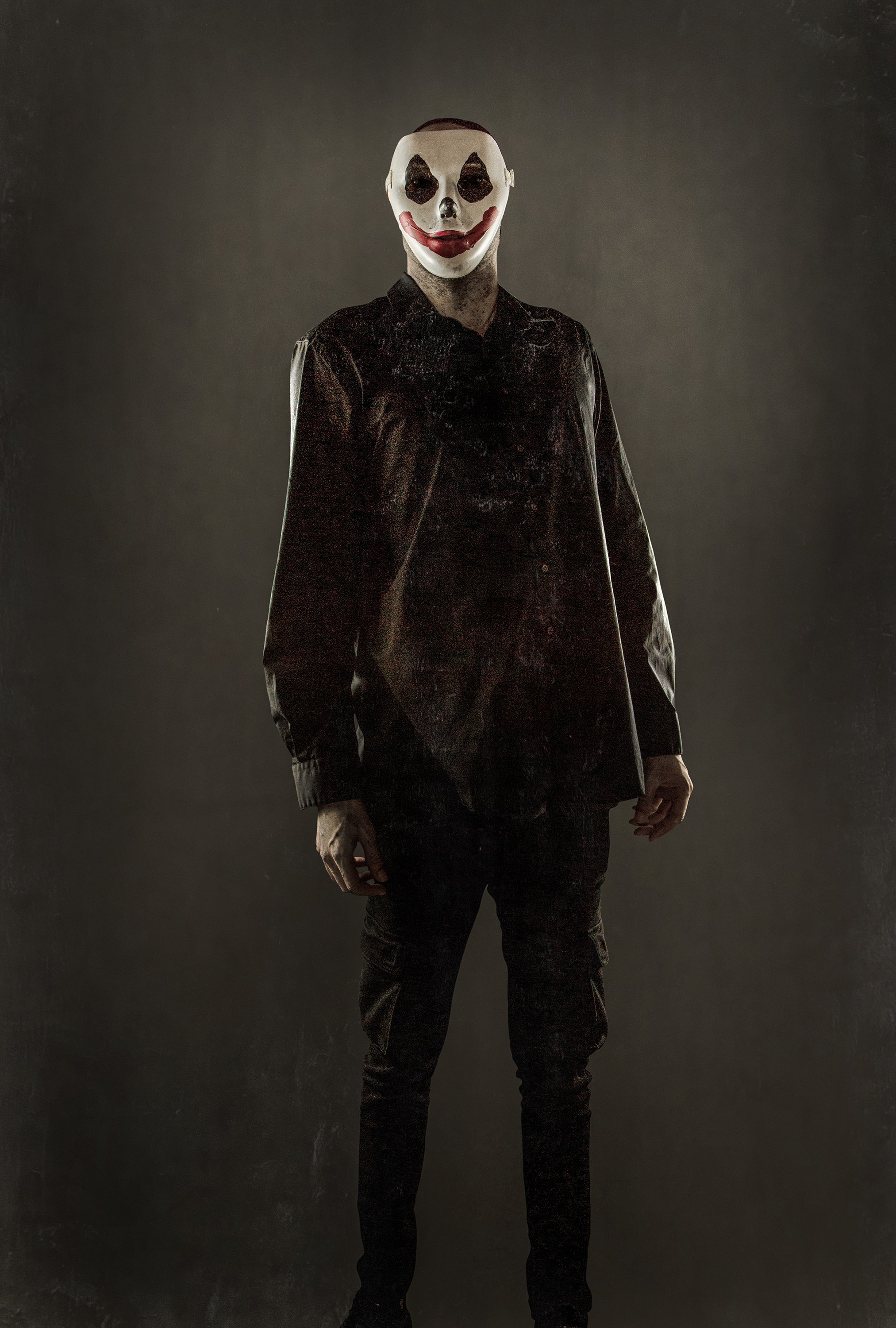 Person wearing a clown mask with exaggerated red lips and black eye makeup, dressed in dark clothing, standing in a dimly lit setting.
