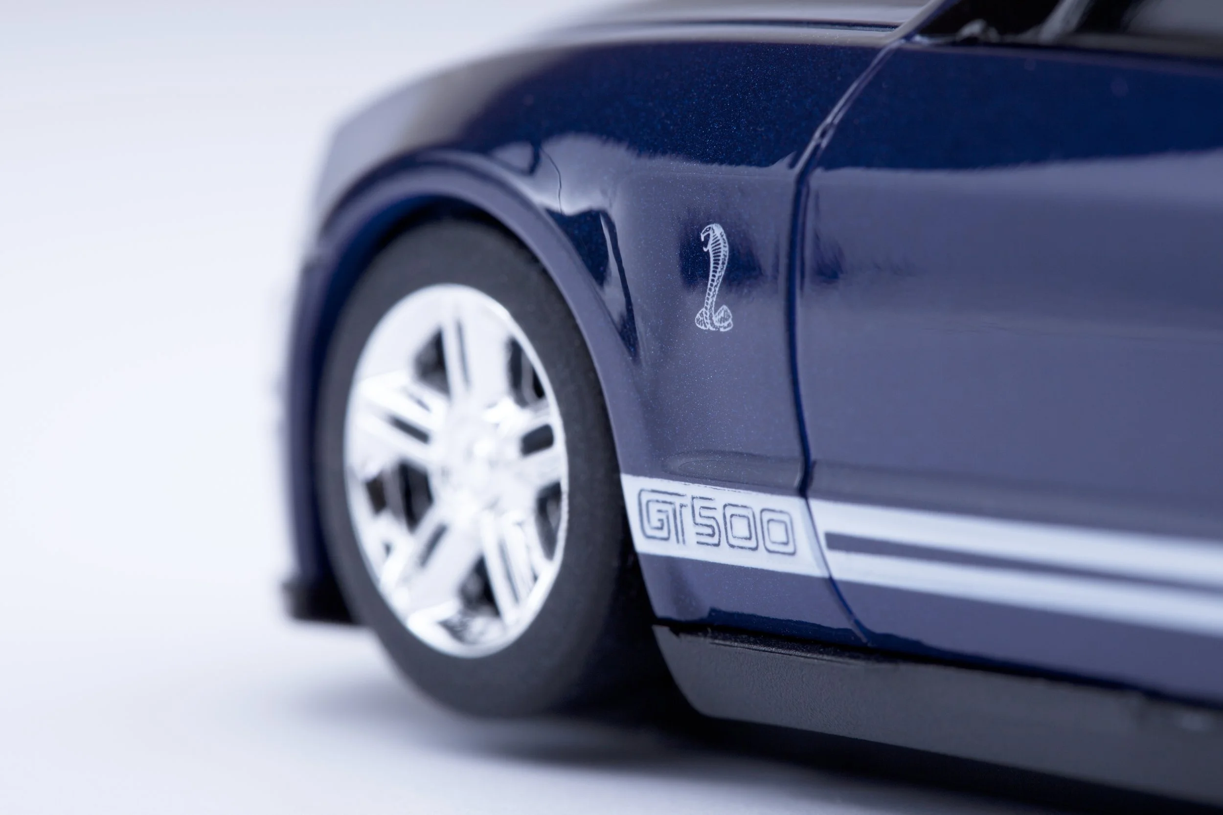 Close-up of a black toy car modeled after a Shelby GT500, with a cobra emblem and 'GT500' label visible on the side.