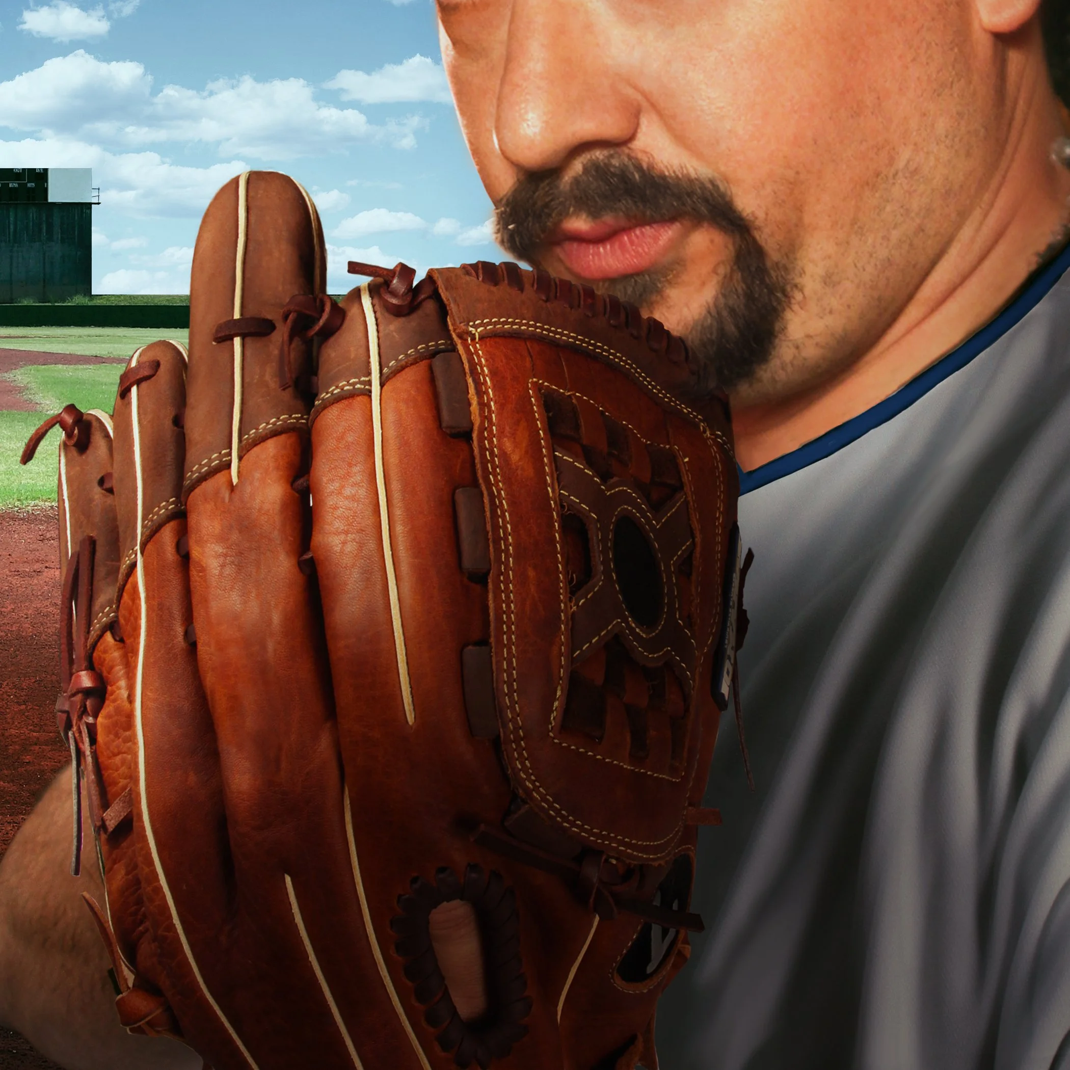 Close-up of a man with a mustache and beard holding a brown baseball glove near his face, on a baseball field with blue sky and white clouds in the background.