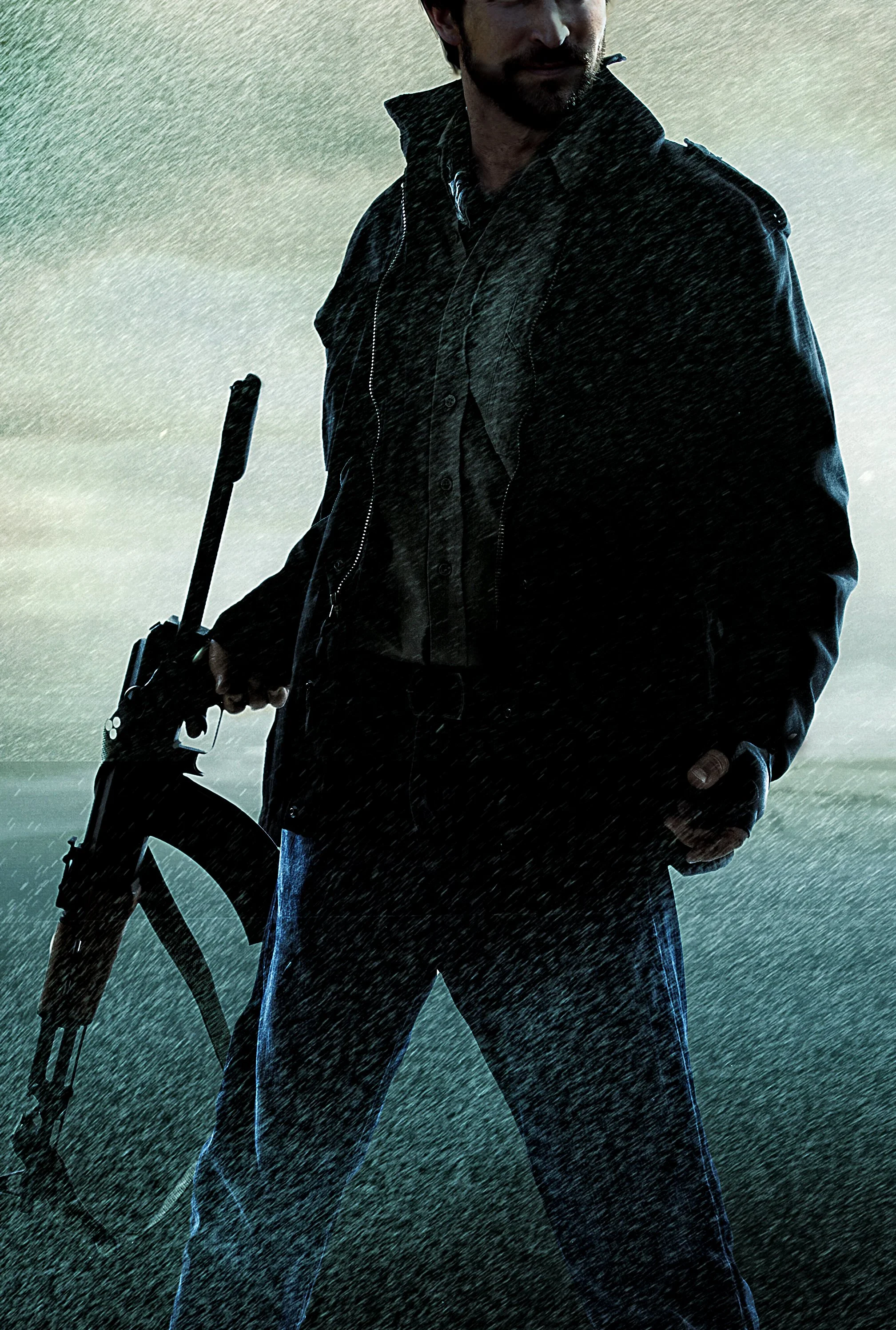 A man with a beard wearing a black leather jacket and blue jeans stands outdoors in the rain, holding a bicycle helmet in his left hand.