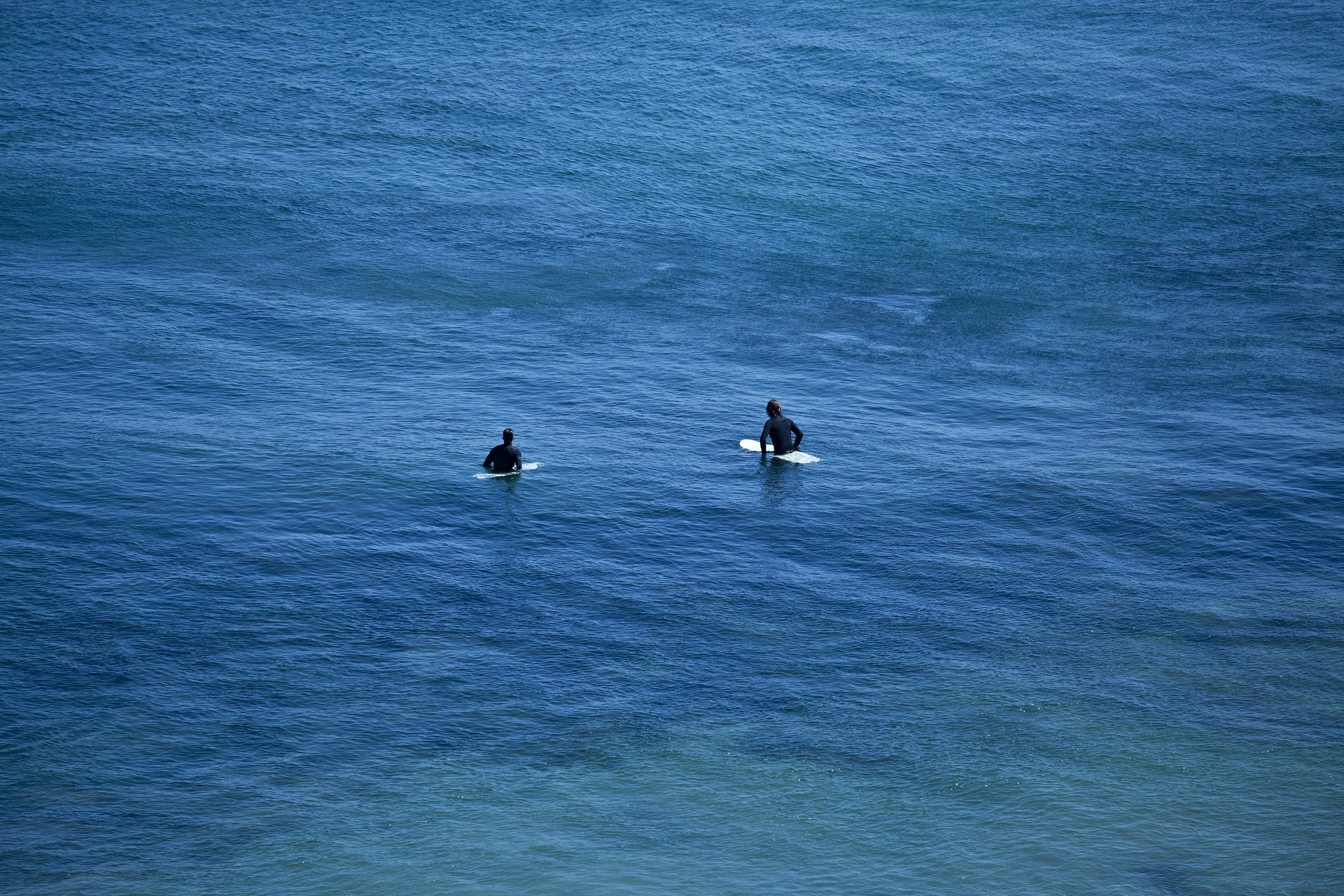 Two surfers paddling on surfboards in a blue ocean.