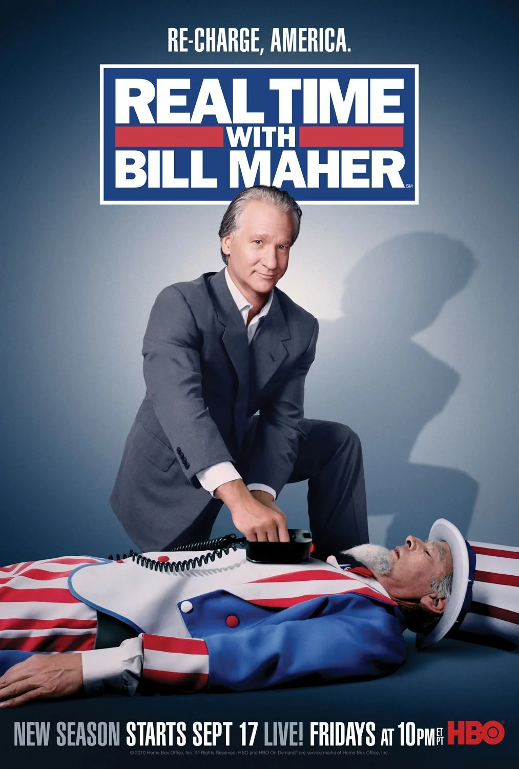 Poster for the TV show 'Real Time with Bill Maher' featuring Bill Maher dressed in a suit, sitting next to a man dressed as Uncle Sam lying on the floor, with a sign above that says 'Re-Charge, America.' The poster announces a new season starting Sep