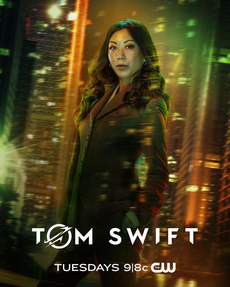 A woman with dark wavy hair wearing a business suit stands in front of a cityscape at night with glowing lights. The image has a futuristic, neon-lit atmosphere. Text on the image reads "Tom Swift," 