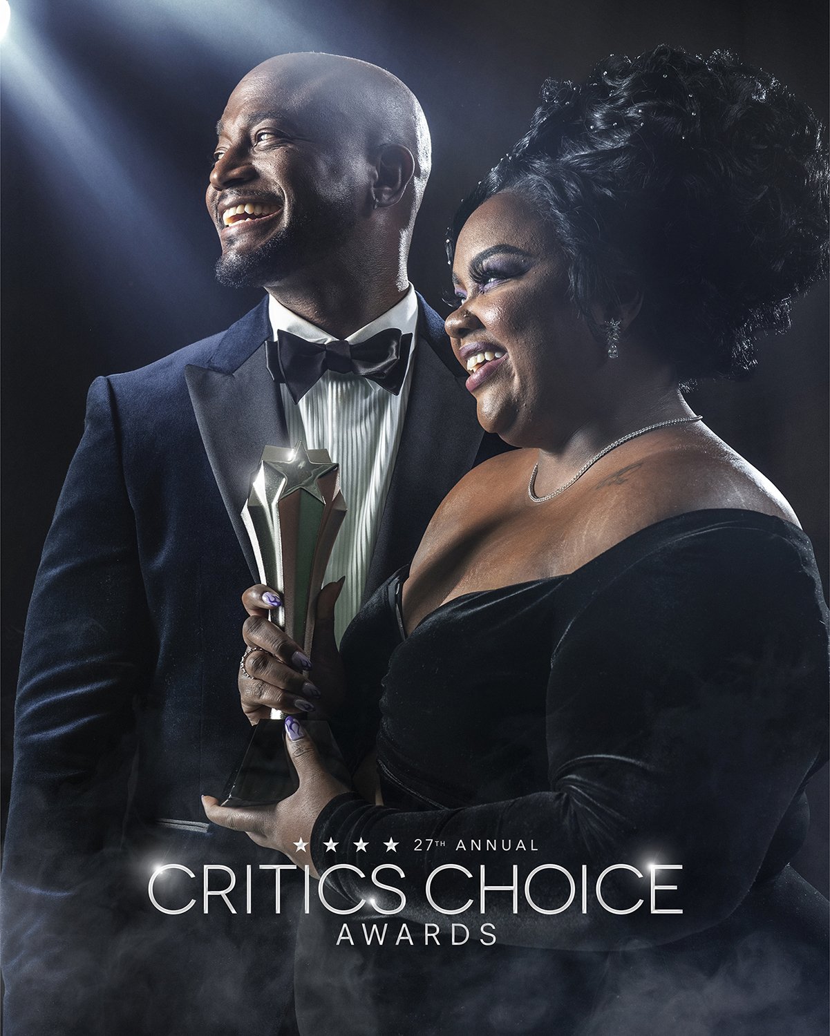 A man and woman in formal attire smiling, with the woman holding an award trophy at the Critics Choice Awards event.