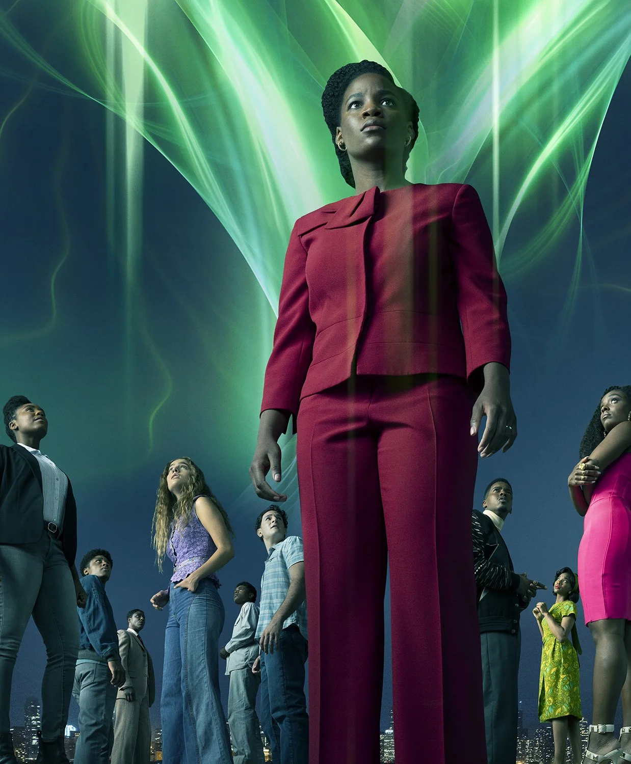 A woman in a red suit stands in the foreground among a diverse group of young people, with green laser-like lights and a dark sky in the background.