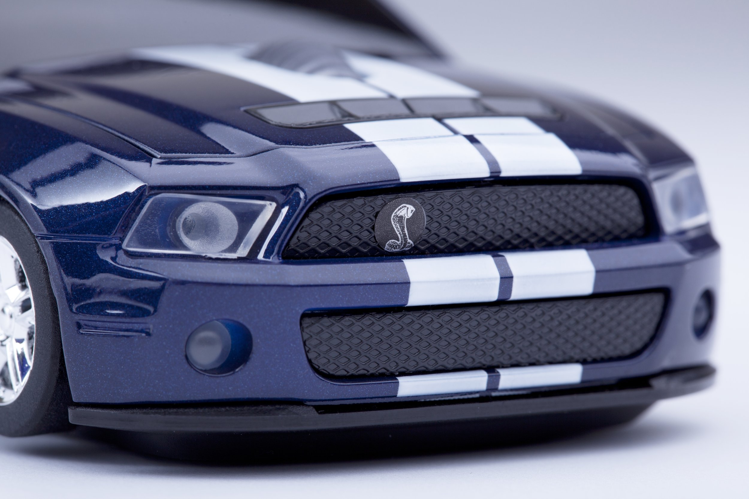 Close-up of a blue toy car with white racing stripes and a Cobra emblem on the grille.