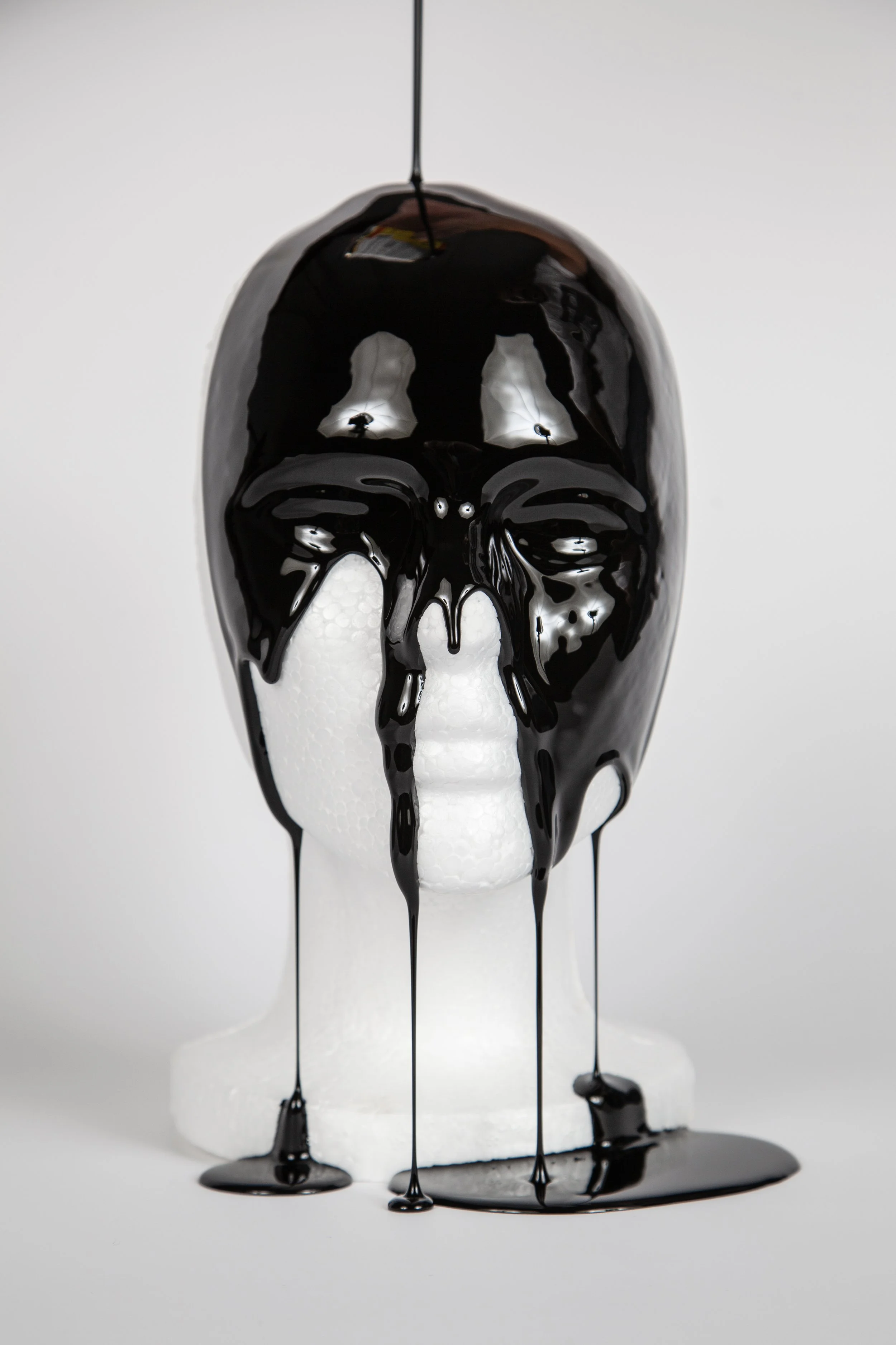 A white styrofoam skull with black paint dripped over it, resembling a melting or dripping skull, on a white background.