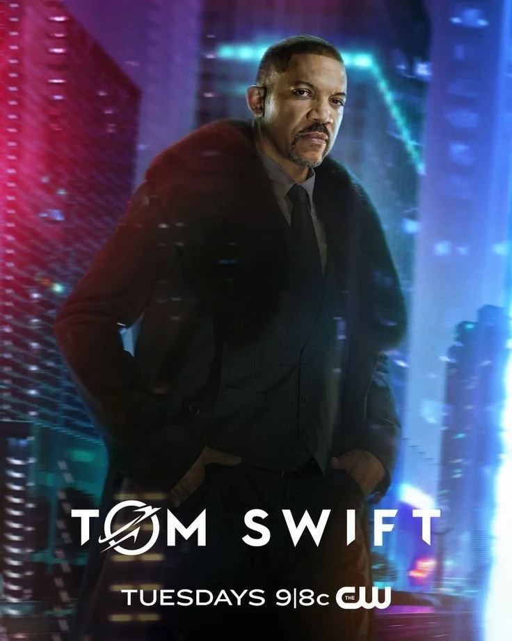 Promotional poster of a man in a suit and jacket, standing in front of a digitally rendered cityscape background with bright lights. Text on the poster includes "TOM SWIFT," "TUESDAYS 9|8c," and the CW logo.