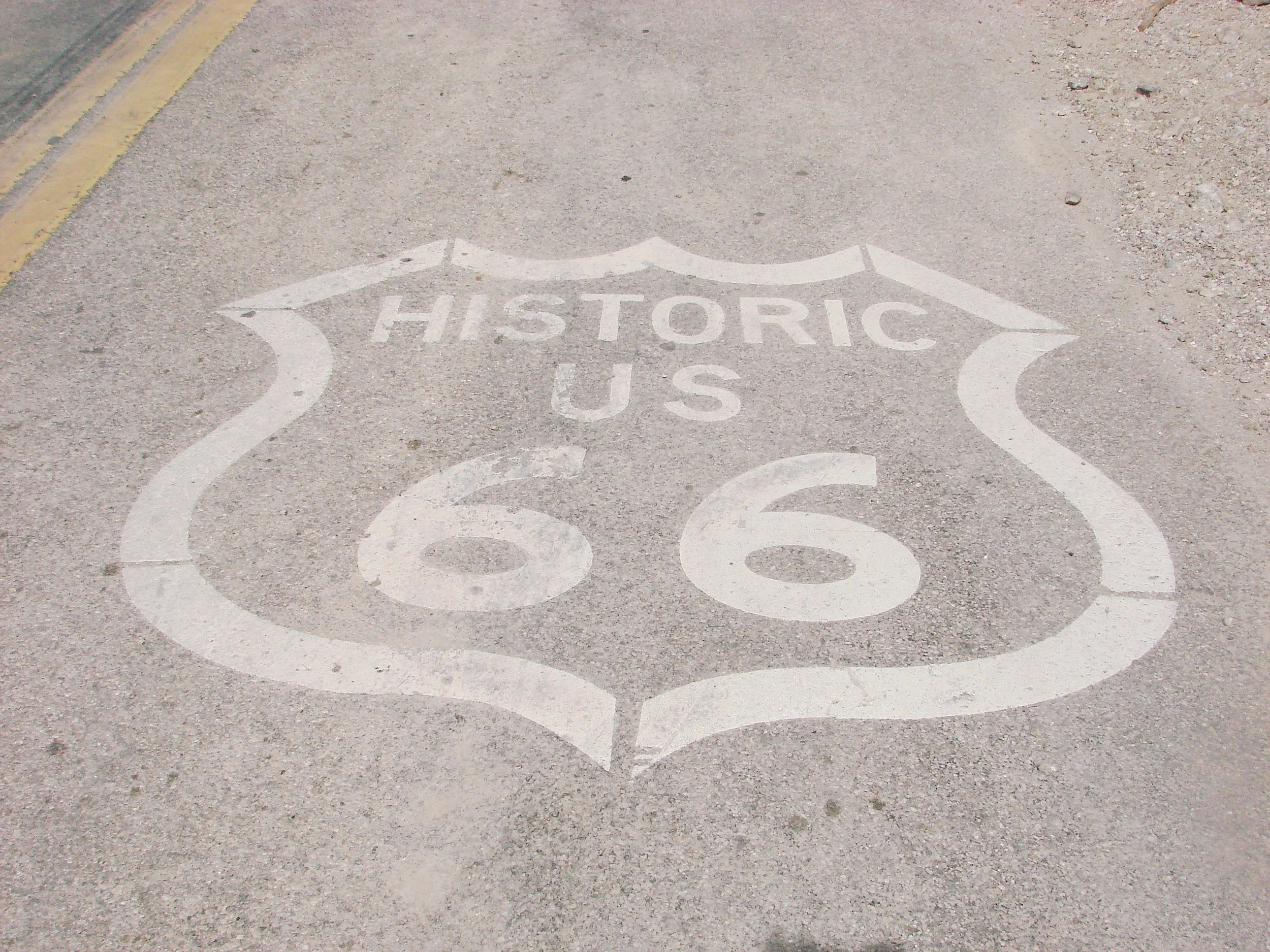 Road with a white painted shield shape with the words 'HISTORIC U.S.' on it. Route 66
