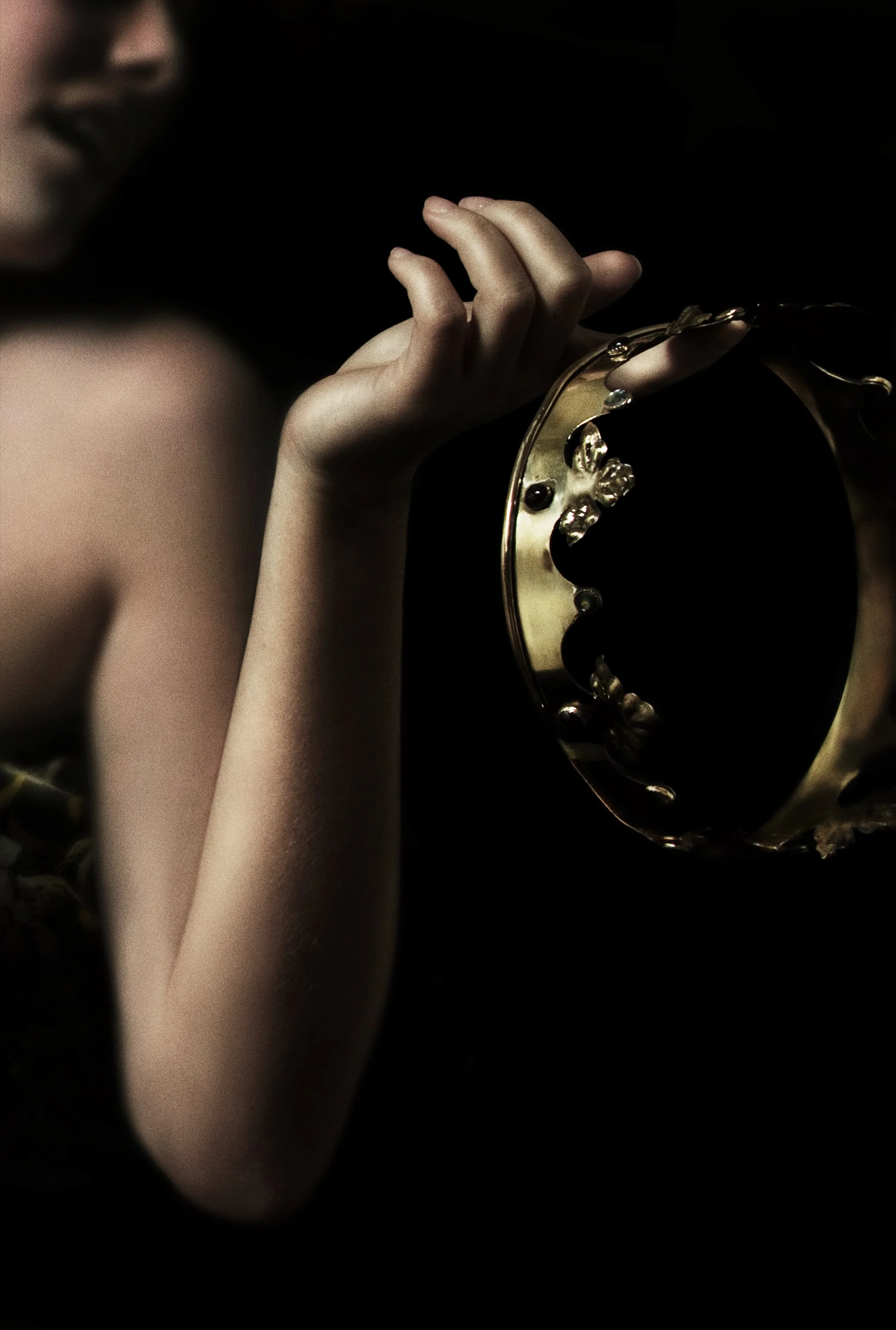 Close-up of a woman's hand holding a gold bracelet with ornate design, visible against a dark background.