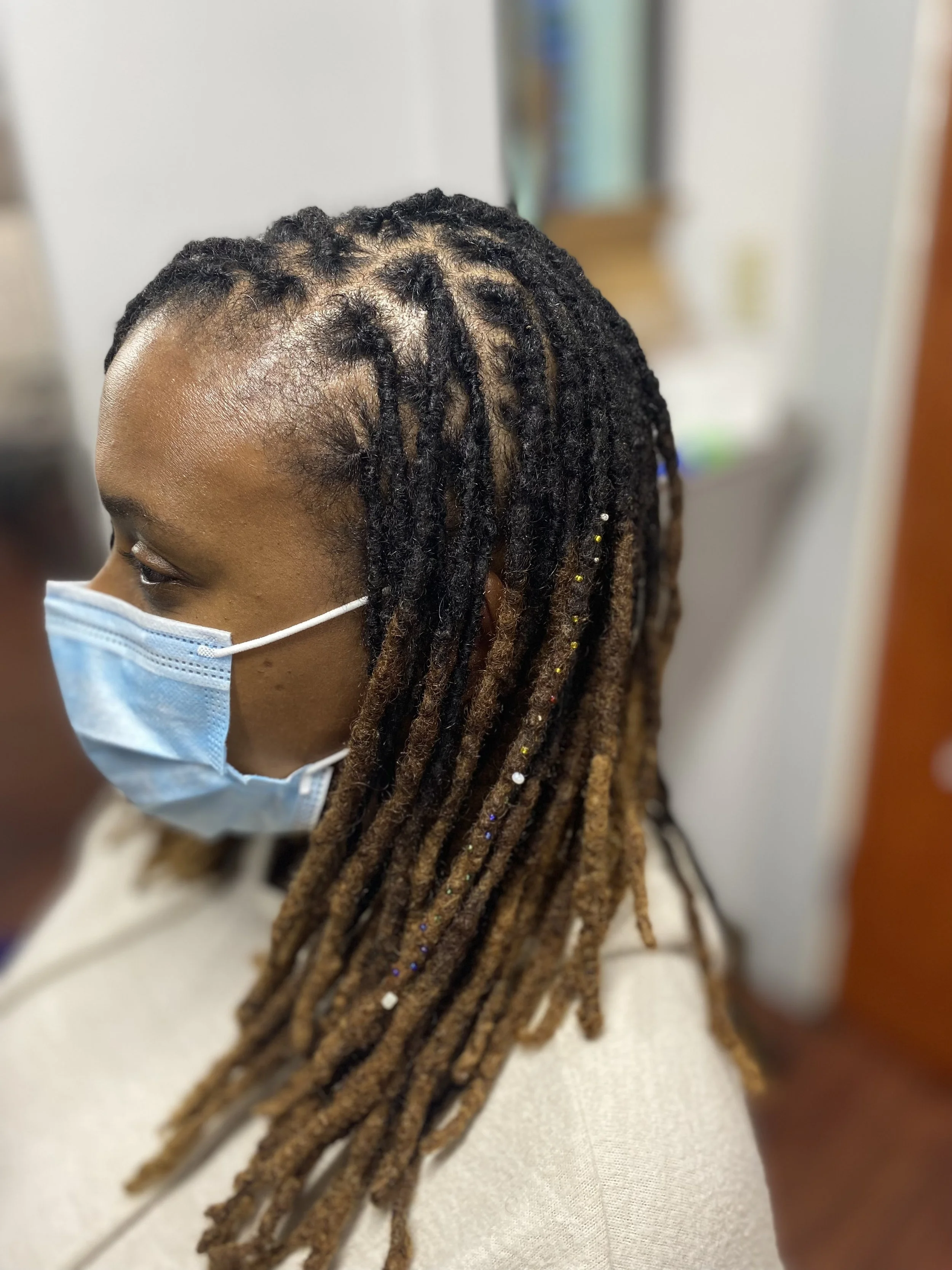 Person with wearing a face mask with styled dreadlocks and hair beads.