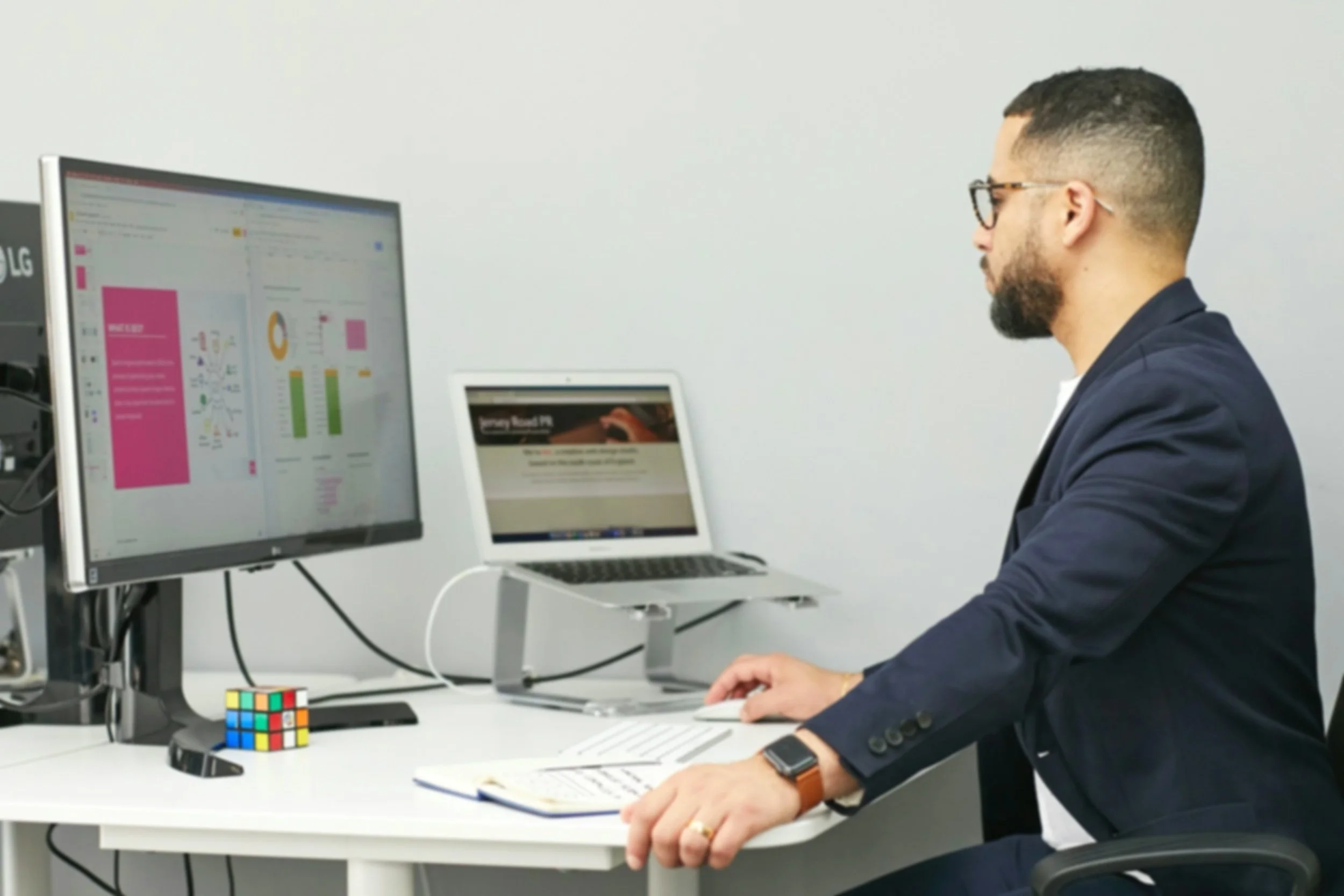 A man viewing two computer screens with analytic chart presentations and text