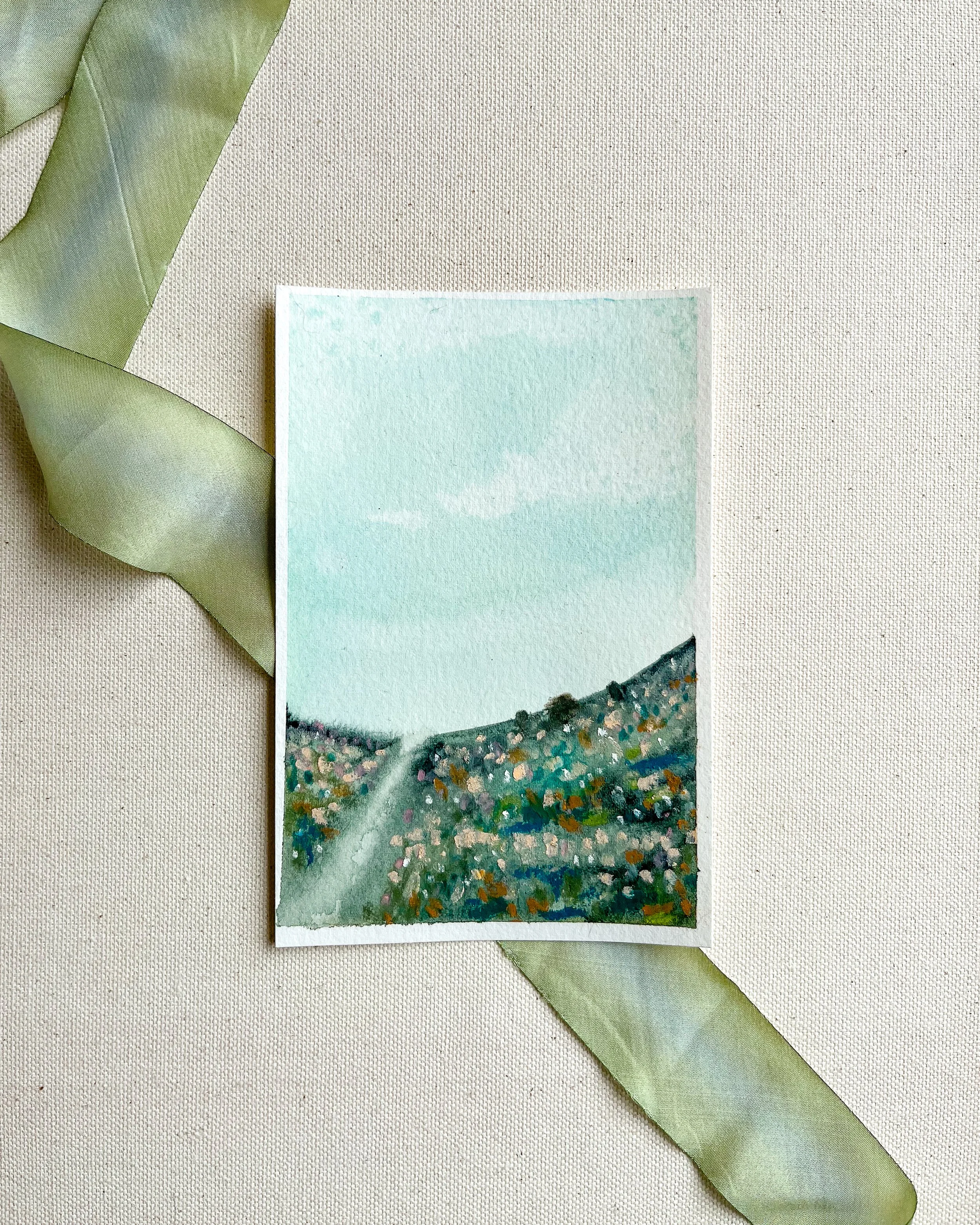 Blue abstract mixed media landscape painting from above atop green silk ribbon