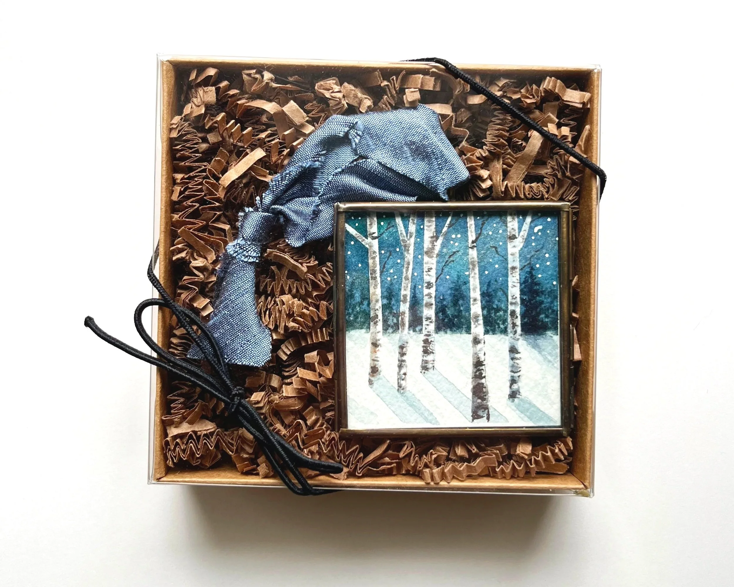 A watercolor painted birch tree ornament in a gift box with black ribbon