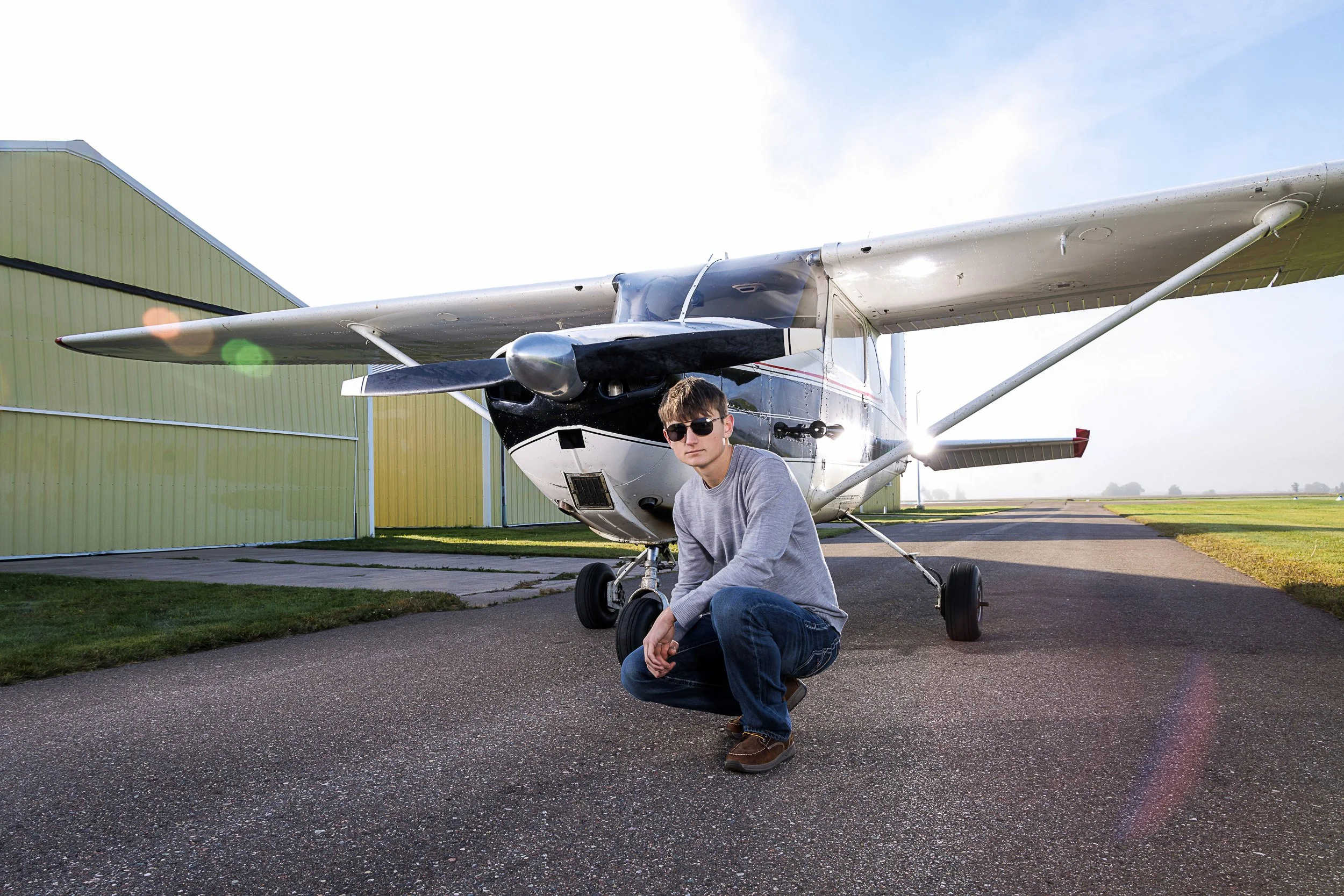 A senior guy posing with his small plane at an airport in Cumberland, WI capturing an adventurous senior photography session.