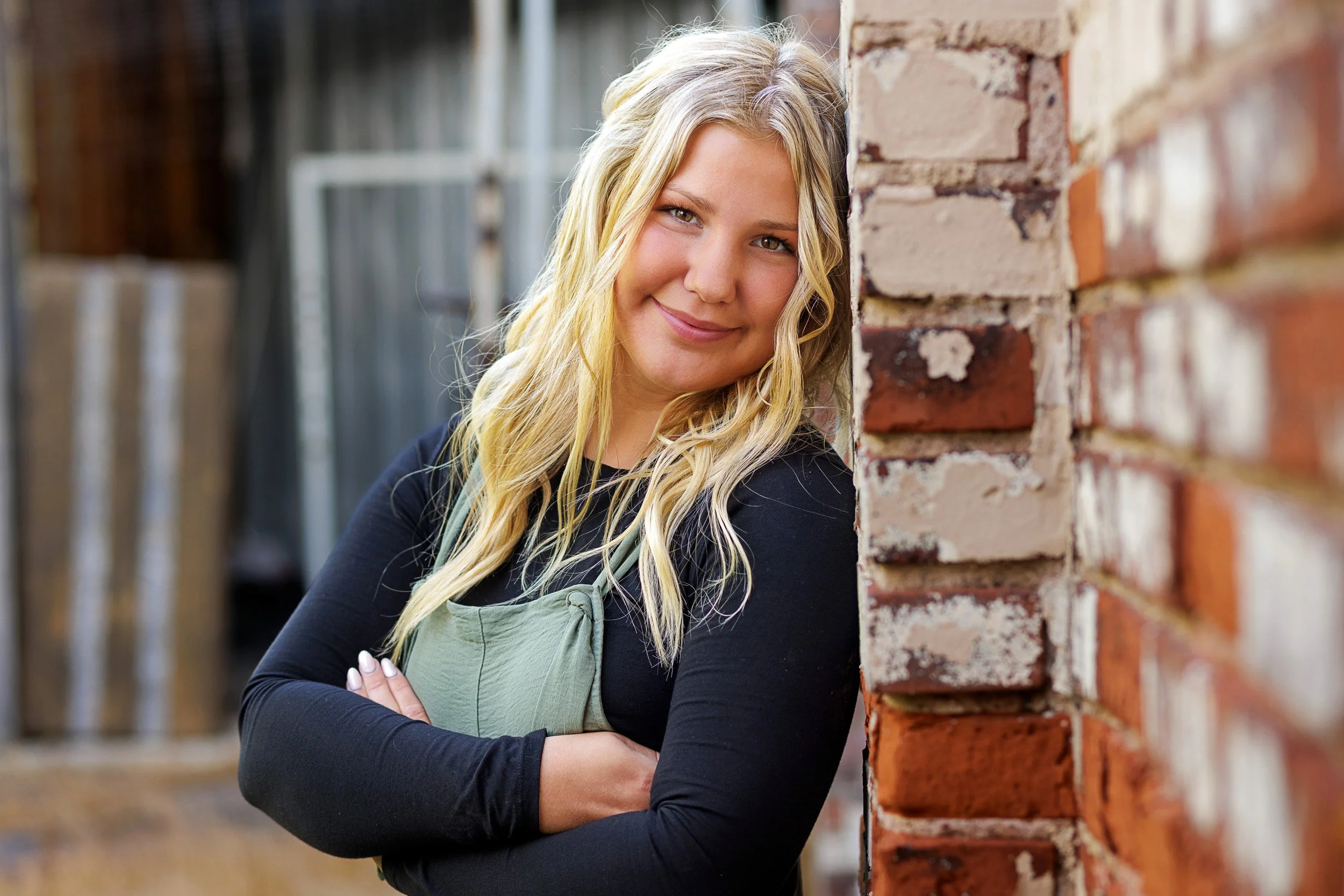 Outdoor senior portrait of a blonde teenage girl by a brick wall in a Rice Lake, WI.