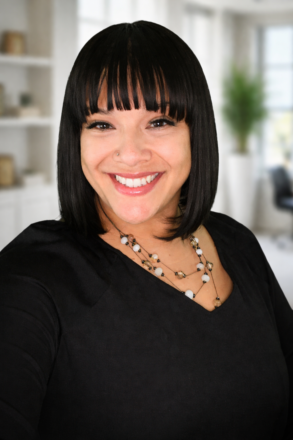 A woman with black hair and bangs smiling in a bright, modern room.