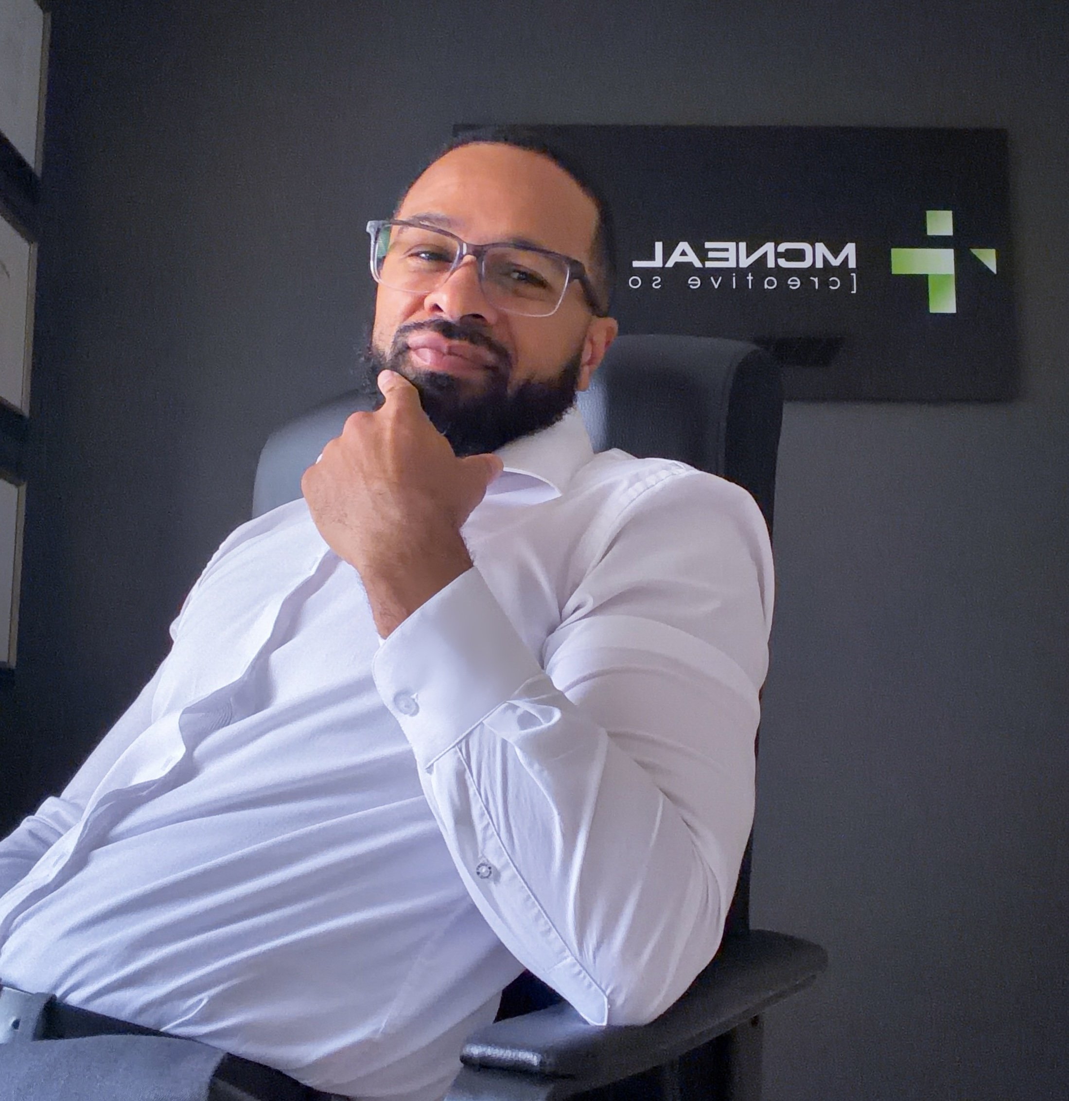 Man with glasses and beard sitting in an office chair with a white shirt, in front of a black wall with a logo for "Medical Creative S.O."
