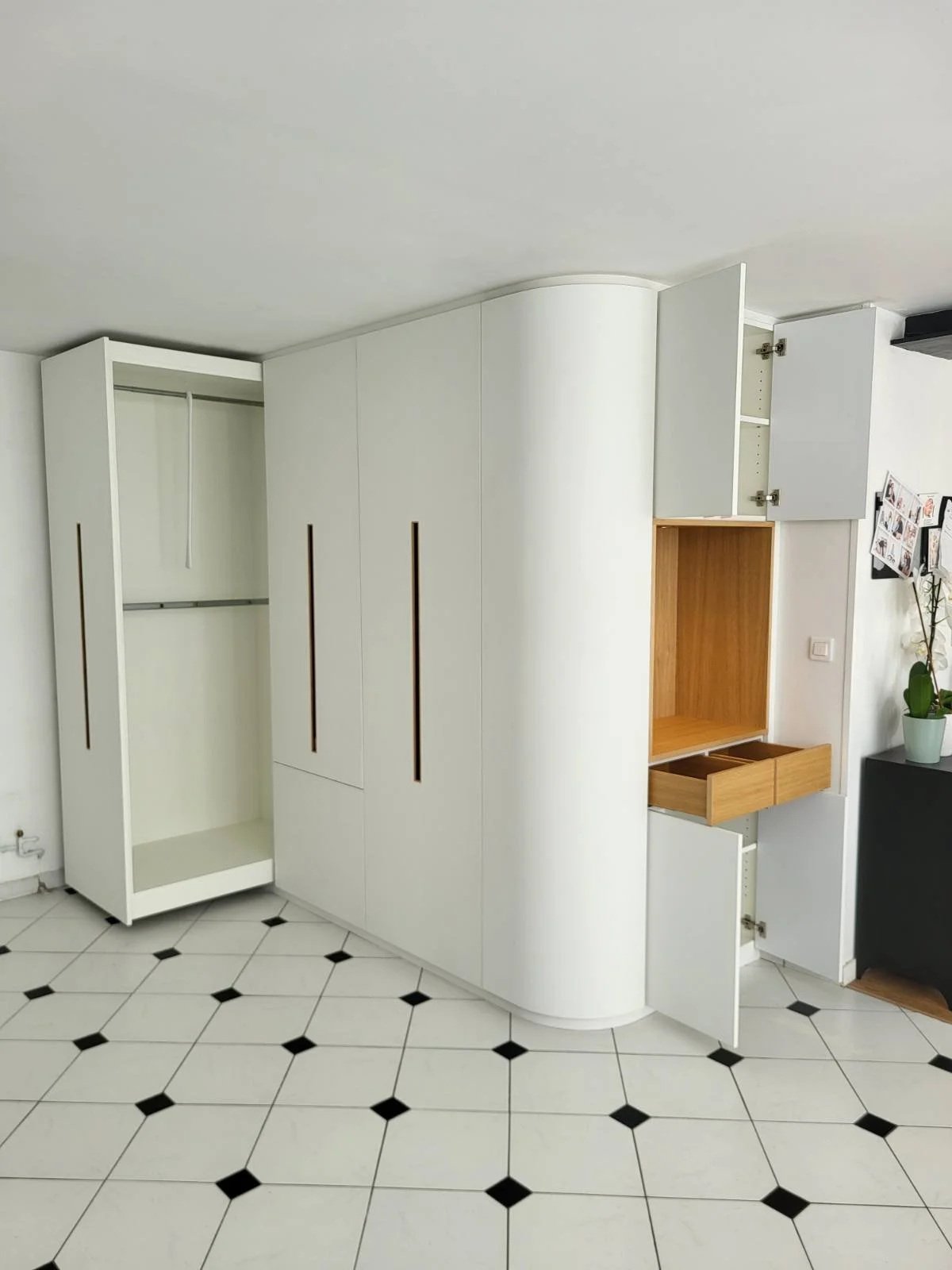 Un dressing d'entrée blanc cintré moderne avec plusieurs portes, certains tiroirs ouverts en bois, situé dans une pièce avec un sol en carreaux blancs et noirs.