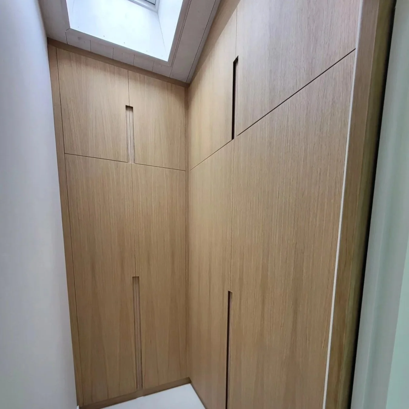Meuble en bois clair avec plusieurs tiroirs et cloisons, situé dans un coin d'une pièce, sous une fenêtre de toit.