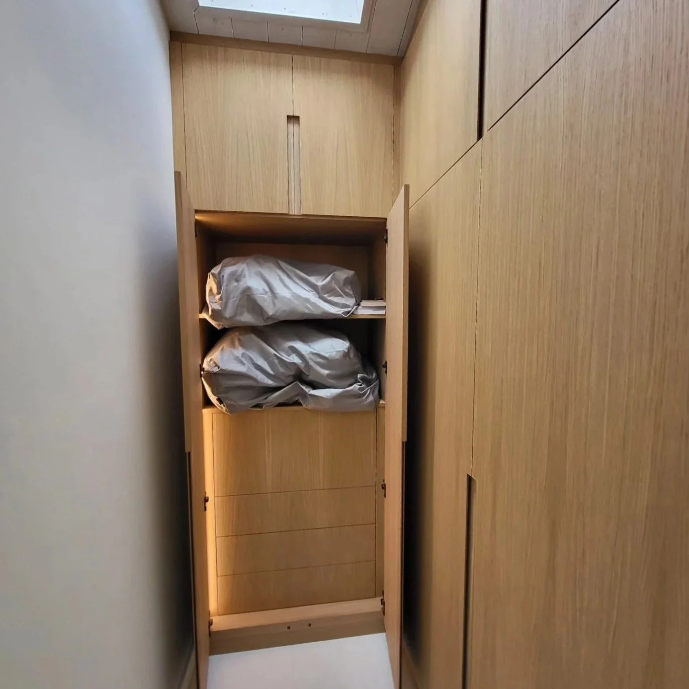 Un meuble en bois avec deux sacs de voyage gris à l'intérieur, situé dans une pièce avec un sol en bois.