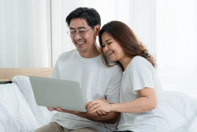 A smiling couple looking at a laptop together in a bright room.