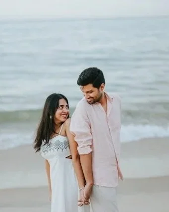 A couple holding hands on the beach, smiling and looking at each other