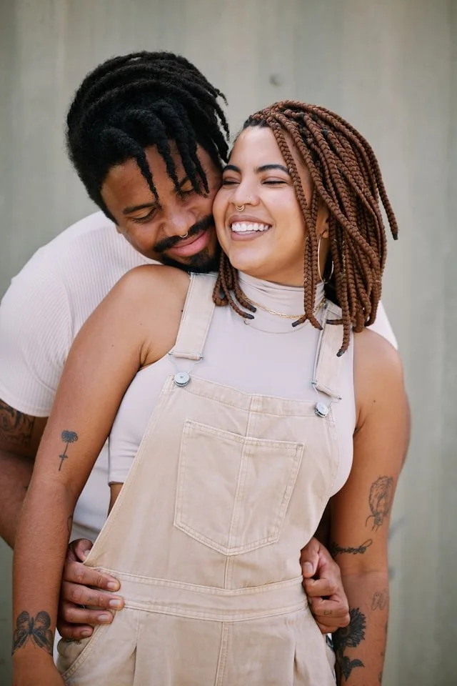 A smiling couple embraces closely, with the man resting his head on the woman's shoulder.