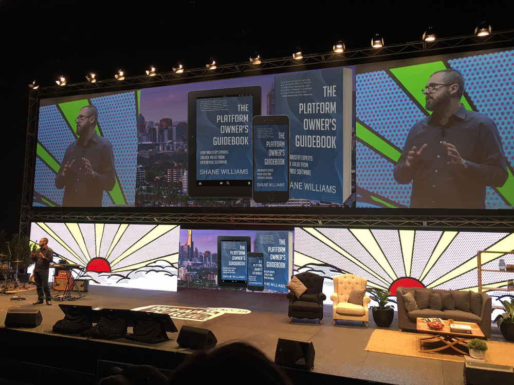 Shane Williams speaking on stage, with his book The Platform Owner’s Guidebook on the screens behind him