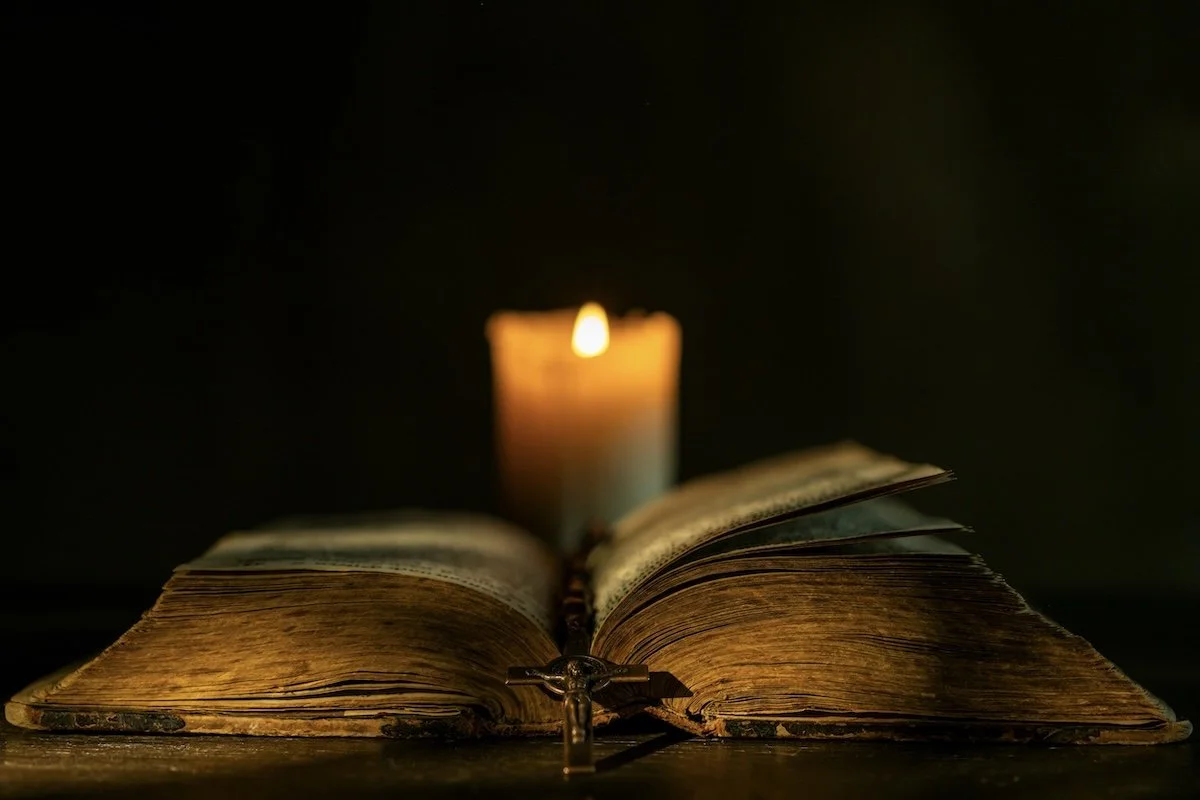 old bible with crucifix and candle illuminating it representing the tradition and truth of the church