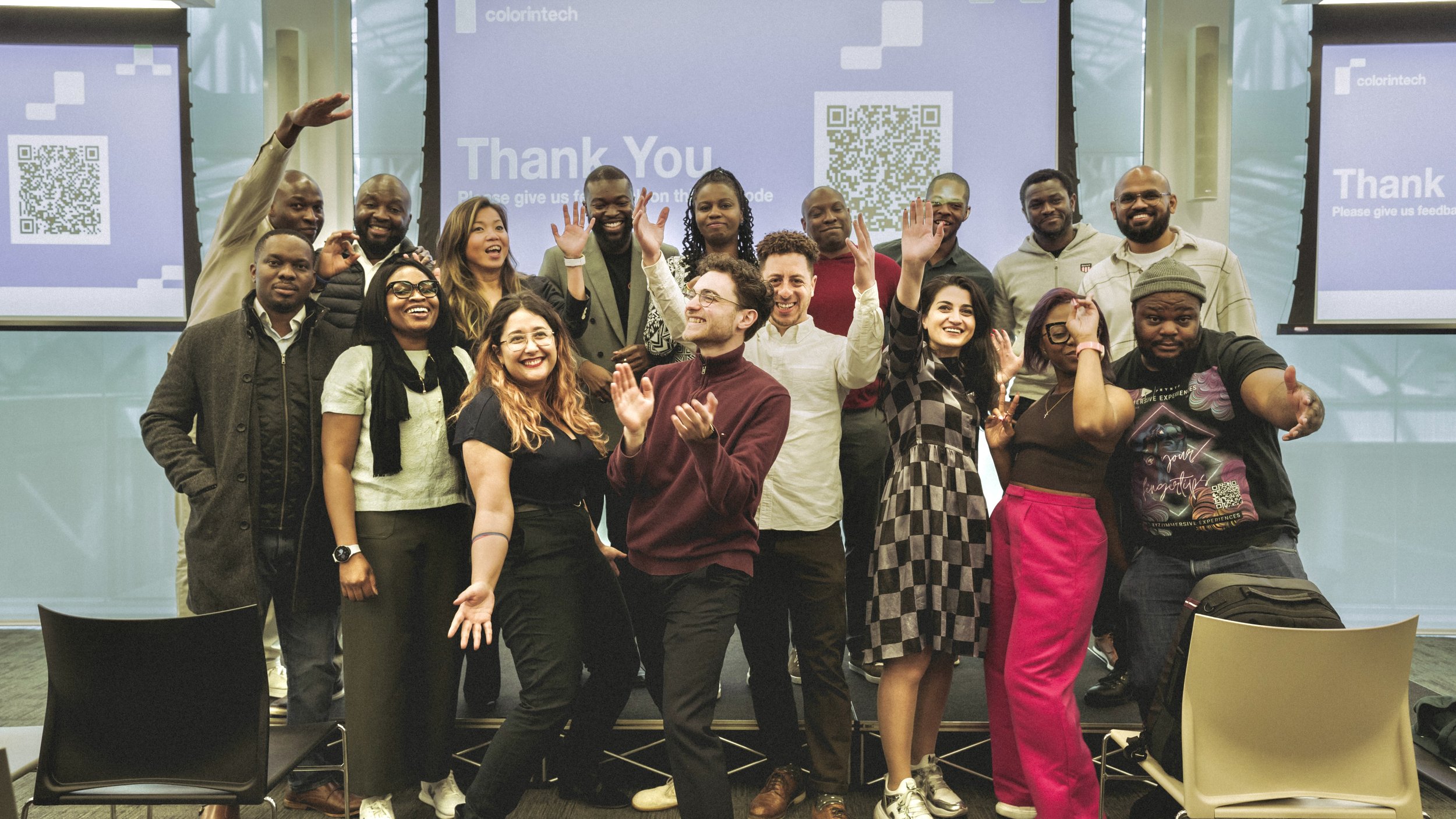Group of diverse professionals celebrating in a conference room with screens displaying 'Thank You' and QR codes in the background.
