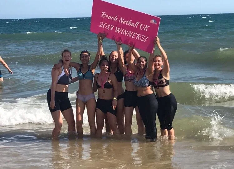 Inglis Netball Club players celebrating the 2017 Beach Netball Win by posing in the sea