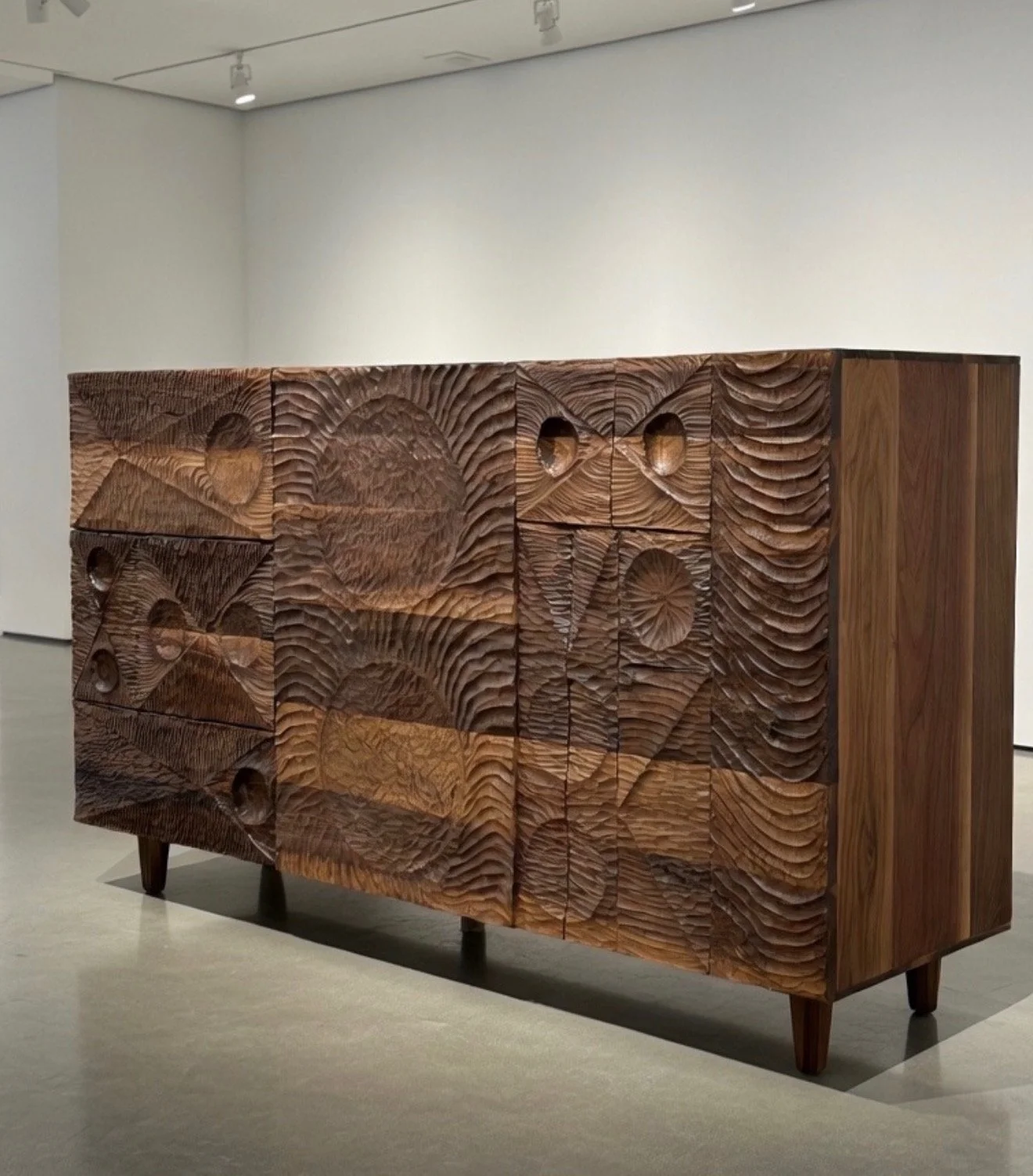 A wooden sideboard with a textured carved surface in an art gallery.