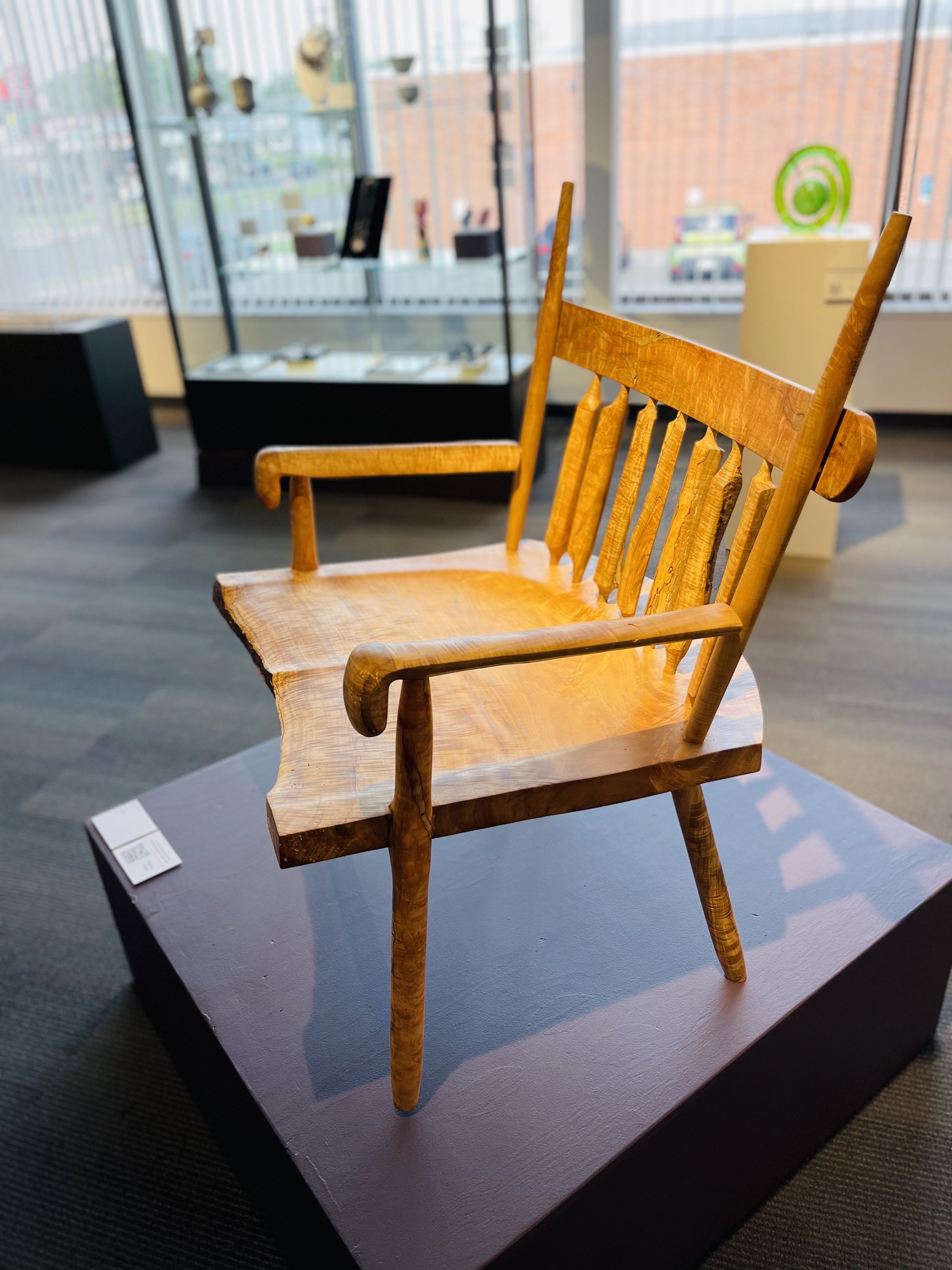 Wooden chair displayed indoors with a display case in the background.