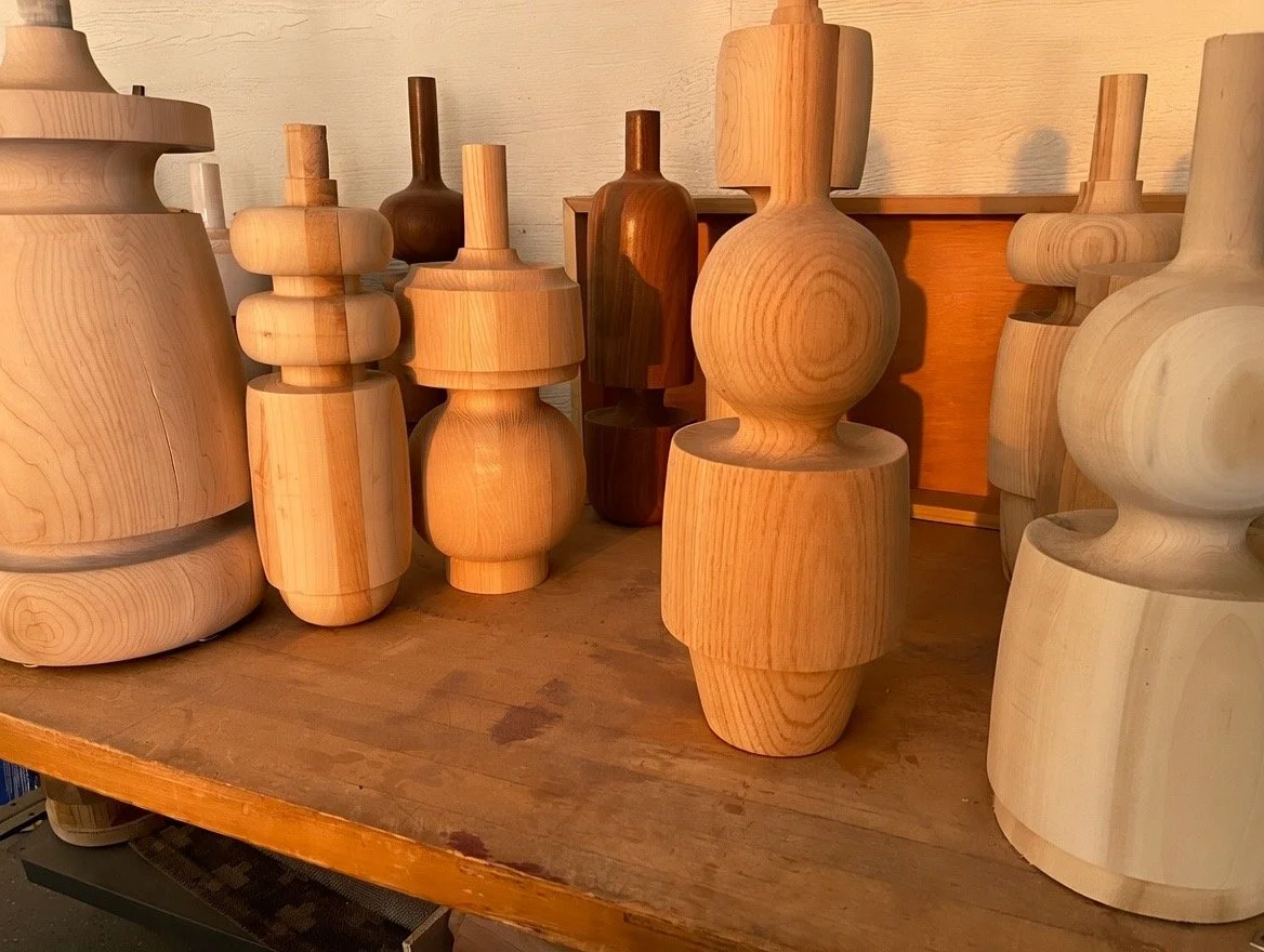 Several unfinished wooden vases and sculptures on a wooden table.