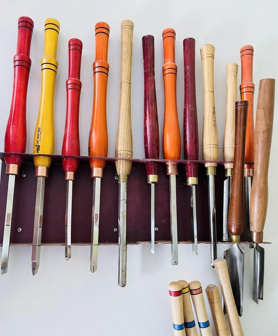 A row of woodworking chisels with colorful handles hanging on a wall.