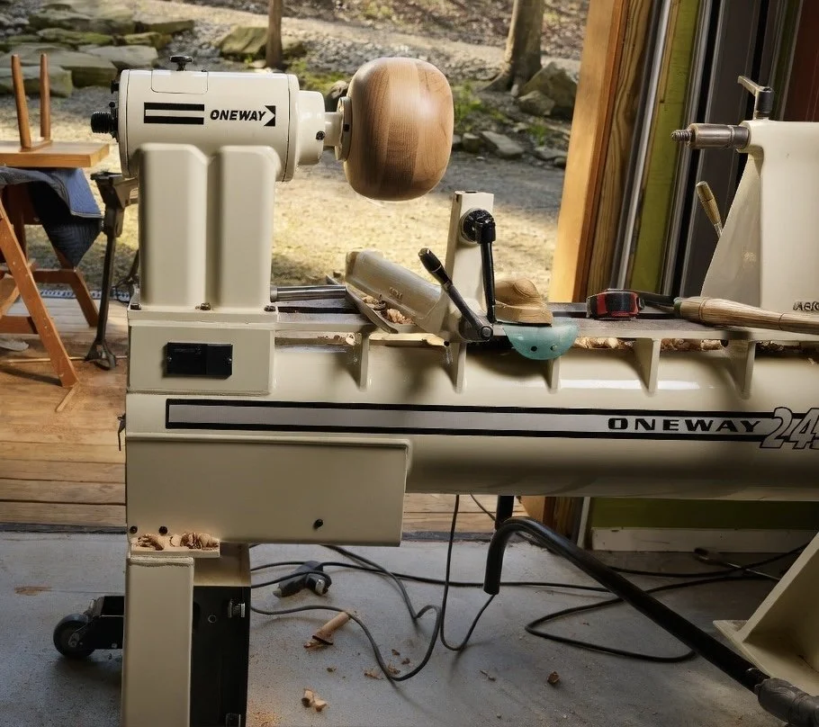 A wood lathe machine in a workshop, with a partially turned wooden piece mounted on it.