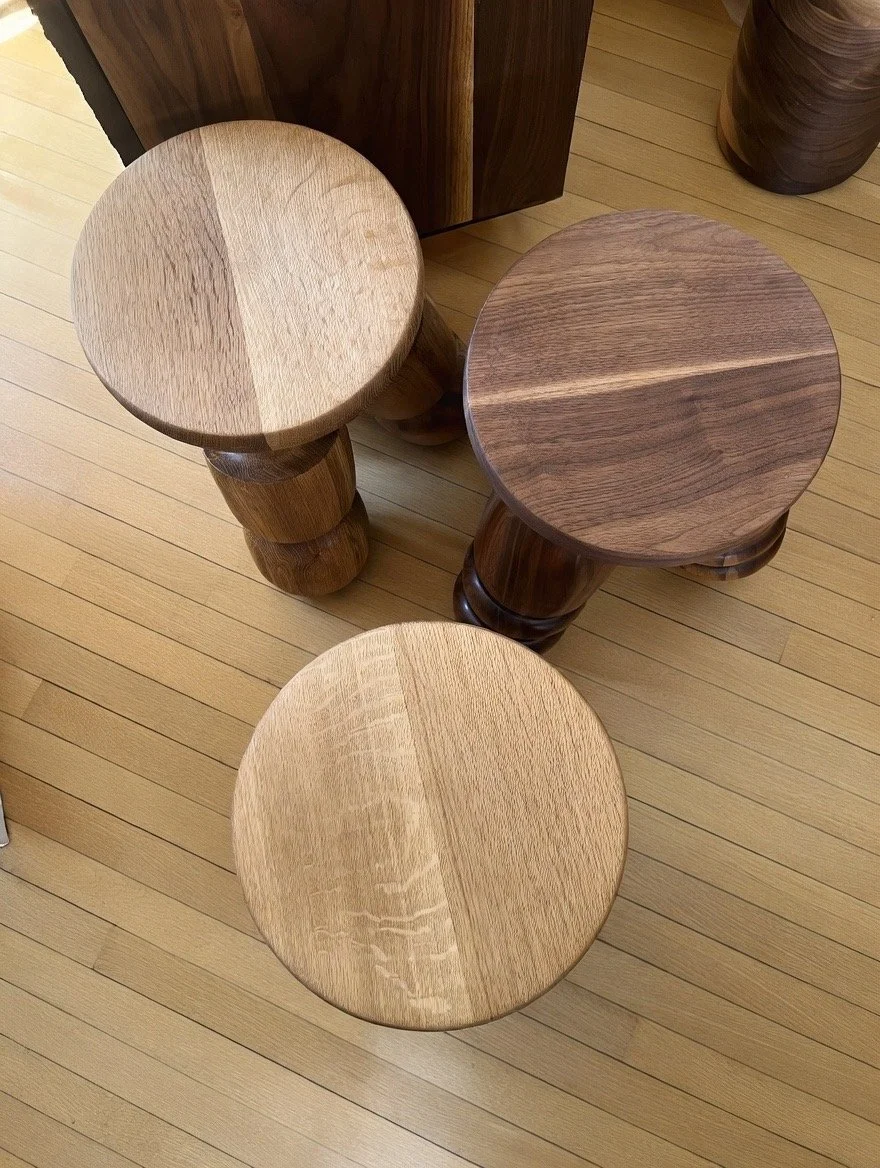 Three wooden stools with round seats and carved legs on a light wood floor.