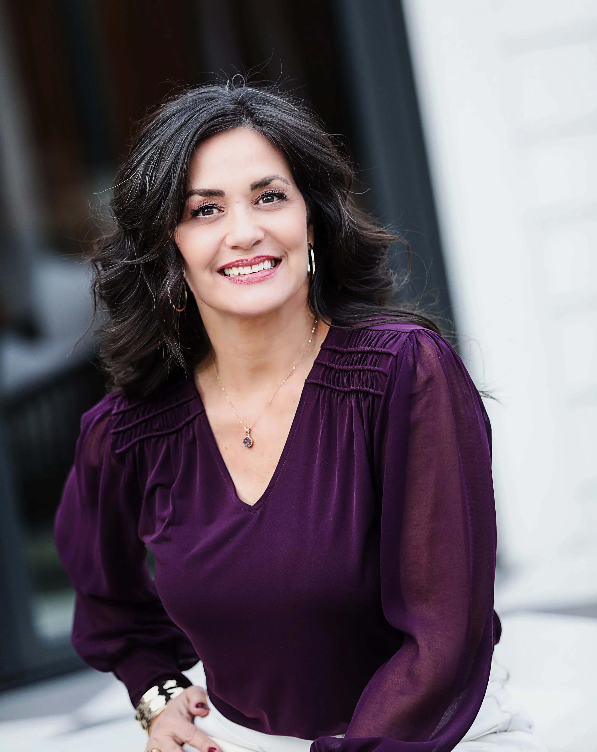 'woman sitting with purple blouse on and smiling