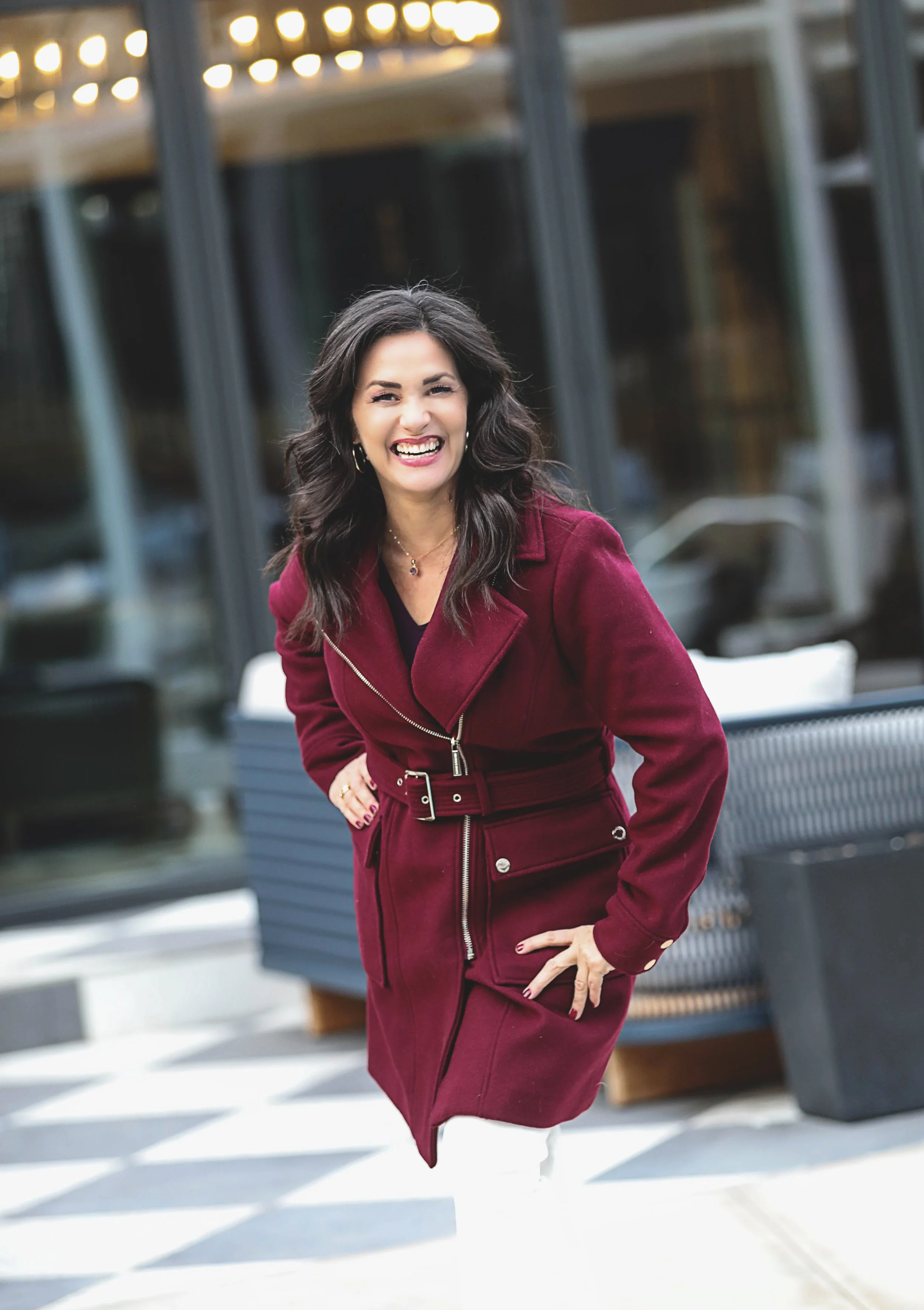 Woman with dark wavy hair wearing a magenta coat smiling