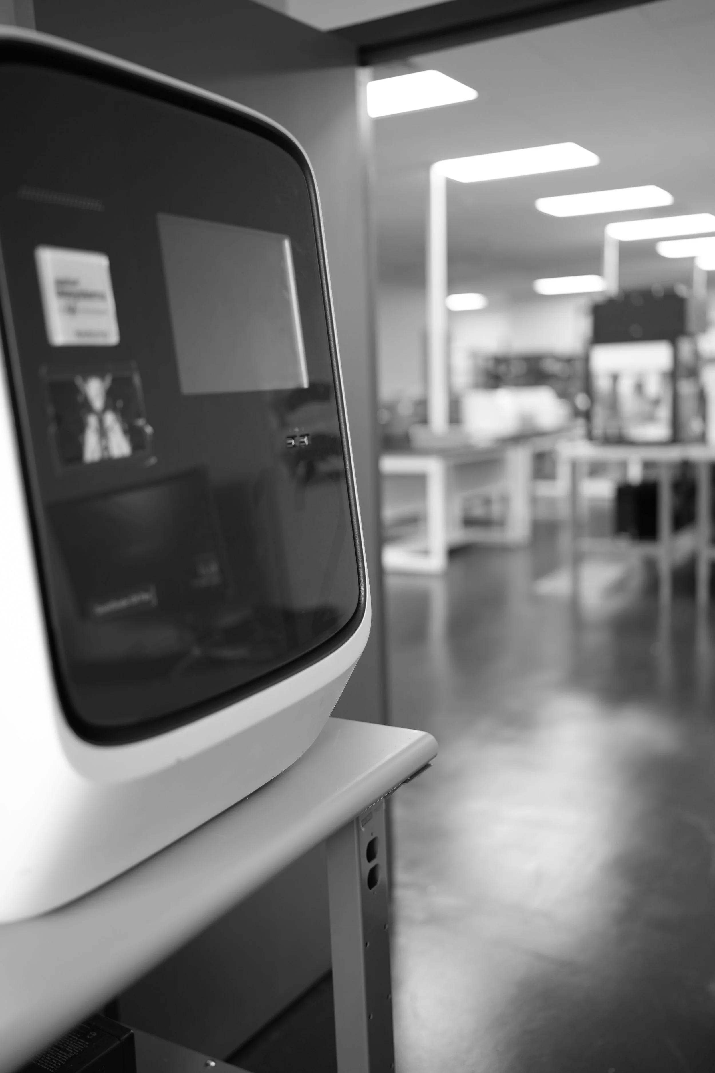 A close-up of a modern self-checkout kiosk in a retail store with an empty screen, in black and white, with the store interior blurred in the background.