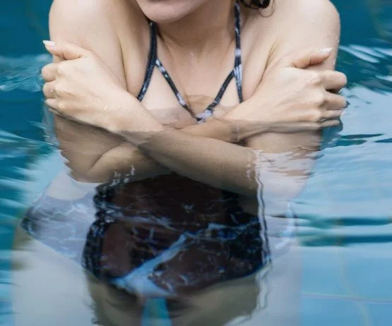 Person wearing a striped swimsuit in a swimming pool with arms crossed over shoulders.