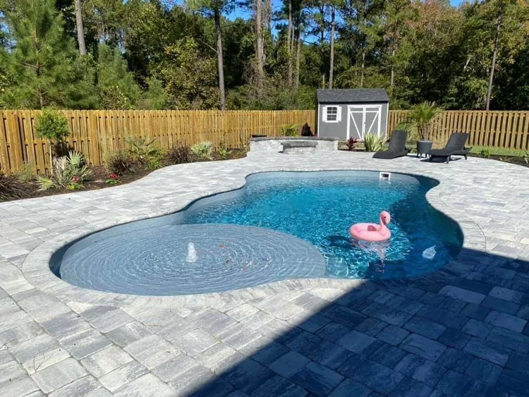 Backyard fiberglass pool with patio seating and landscaping