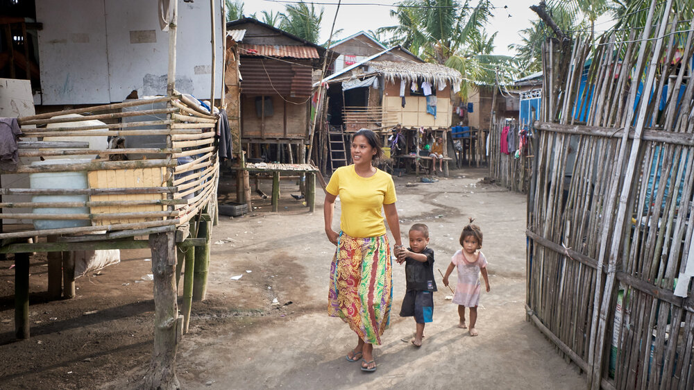  A mother and two children walk between the nipa huts in Barra. These huts are built on bamboo posts with plywood walls and corrugated metal roofs. 