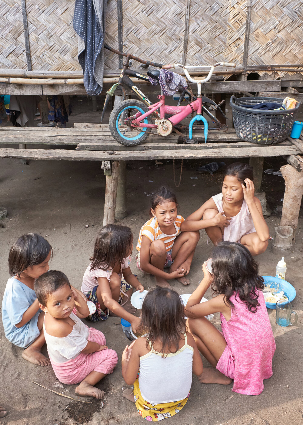  Children sitting on the dirt and eating outside a nipa hut. Barra, Philippines. 