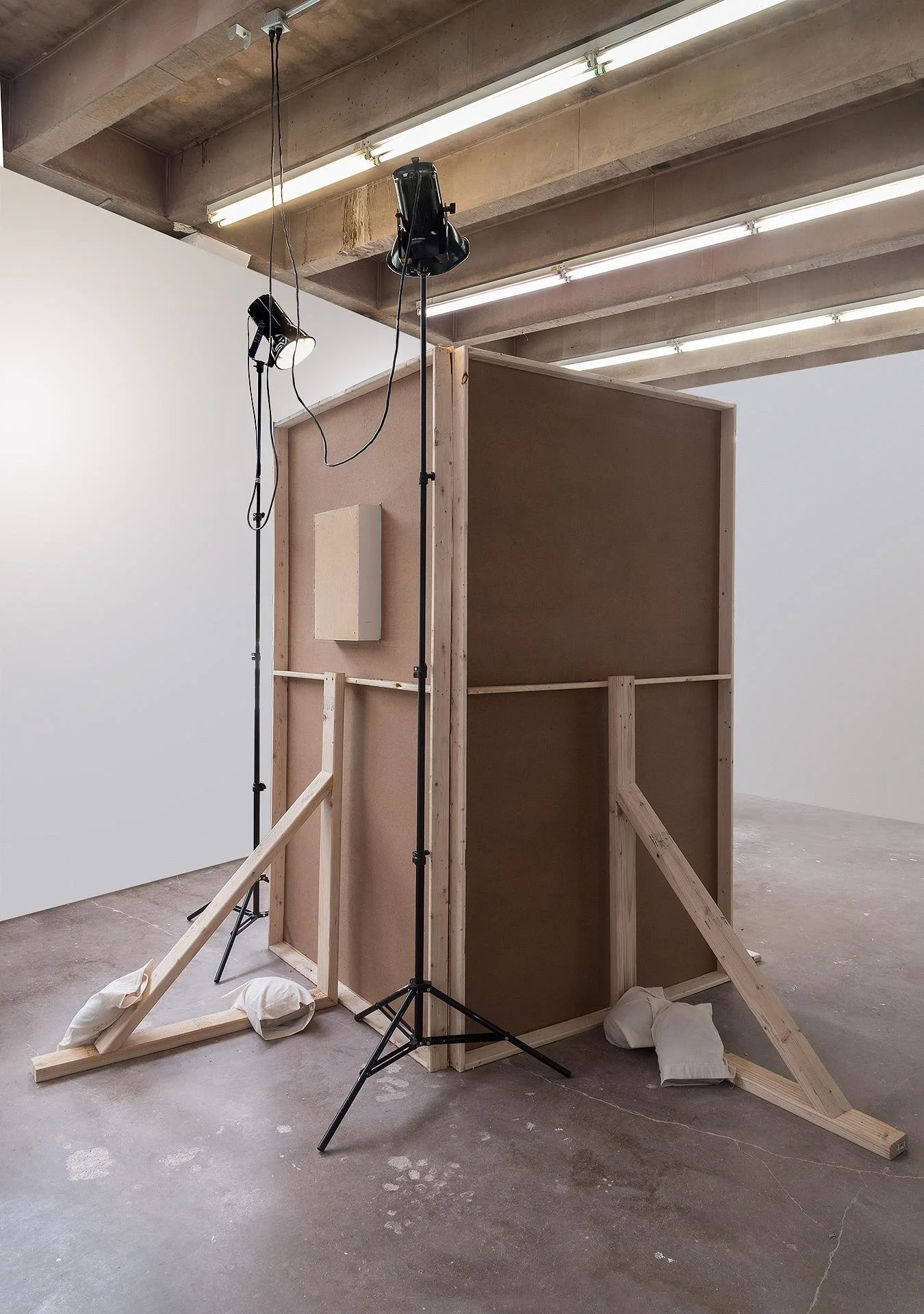 A rear-view of the installation, where you can see the lighting equipment, raw wood, and sandbags holding up the constructed bathroom set.